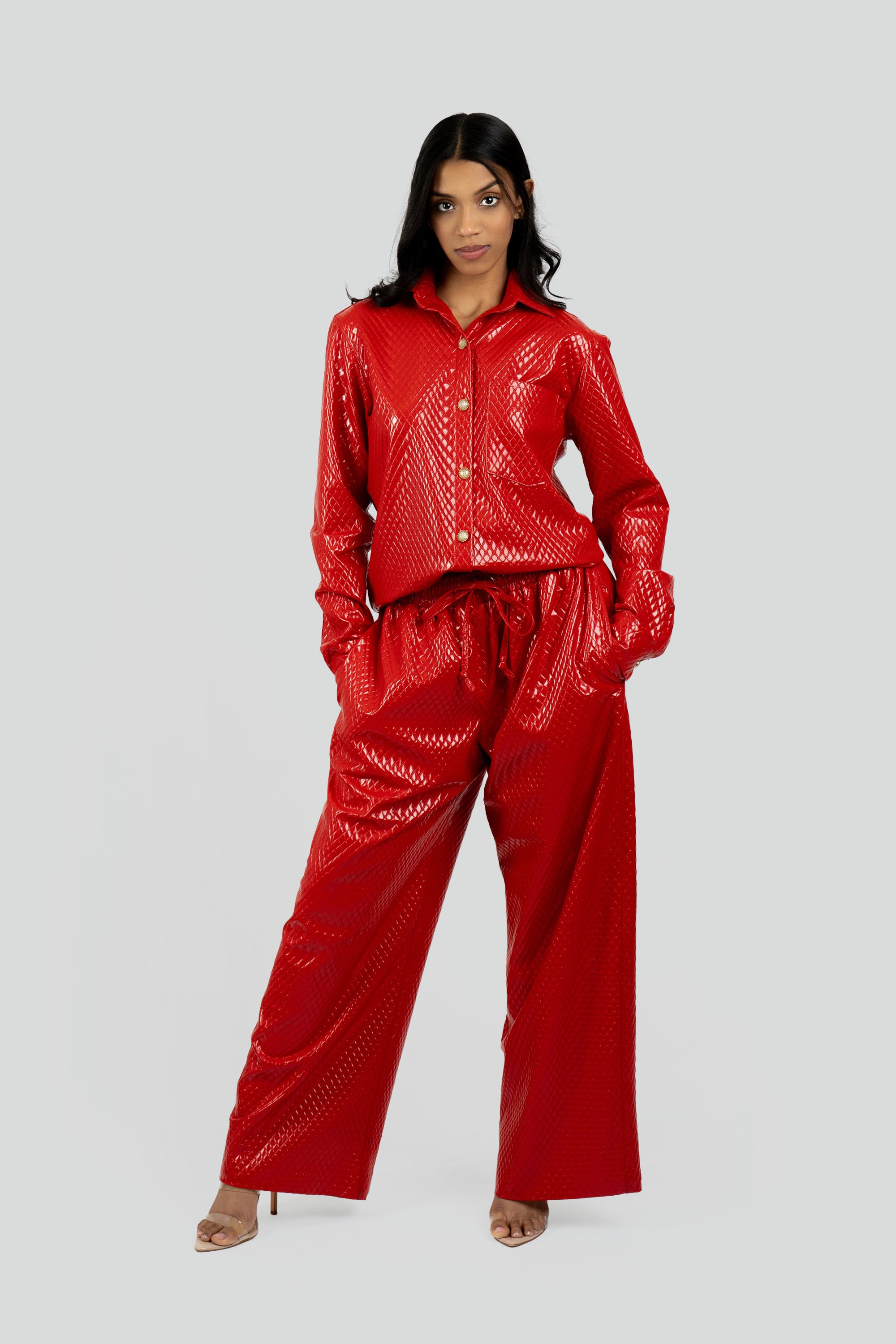 Woman wearing a red textured button up top and matching pants on a plain background