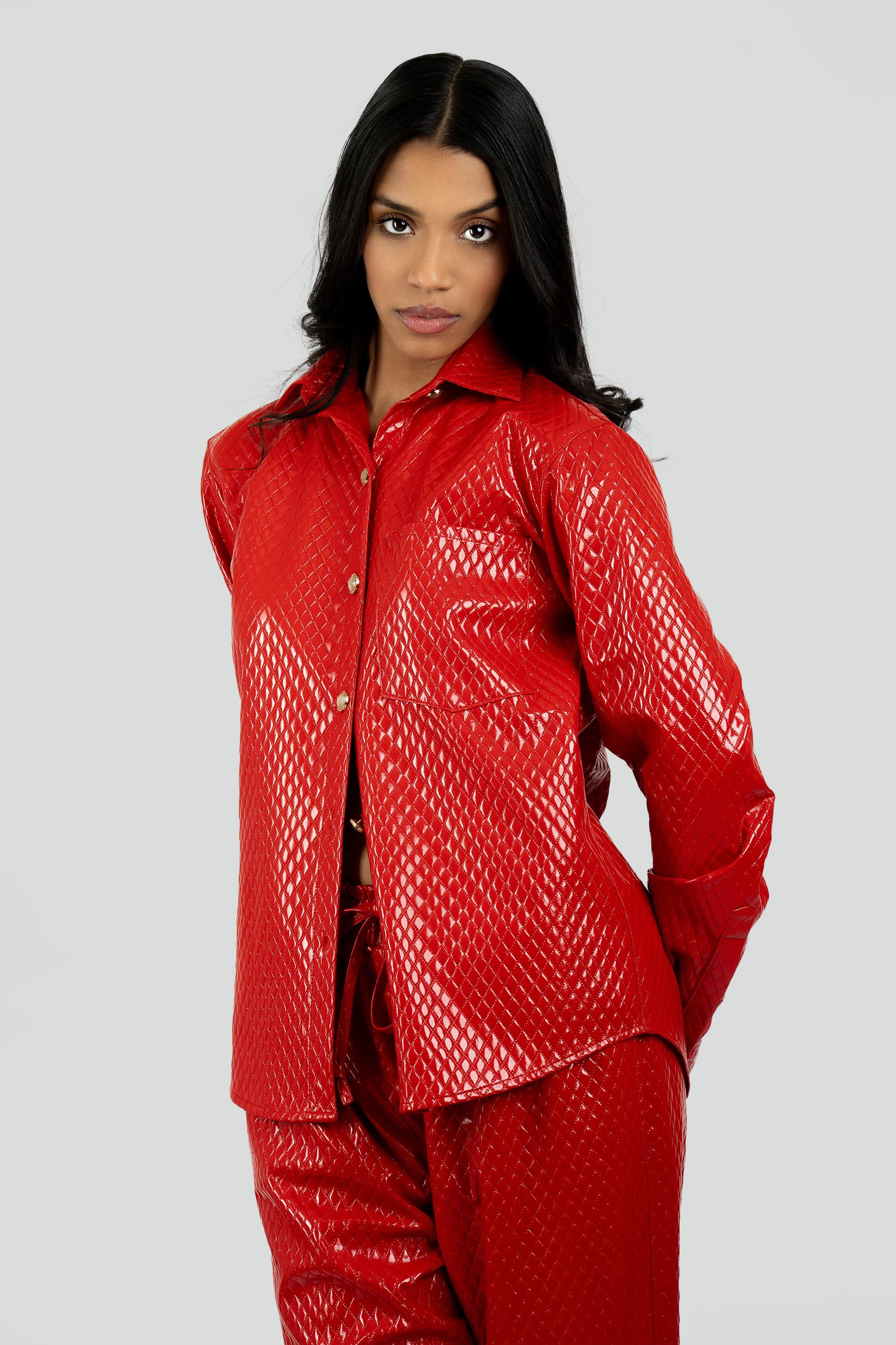 Woman wearing a red textured button up top and matching pants on a plain background