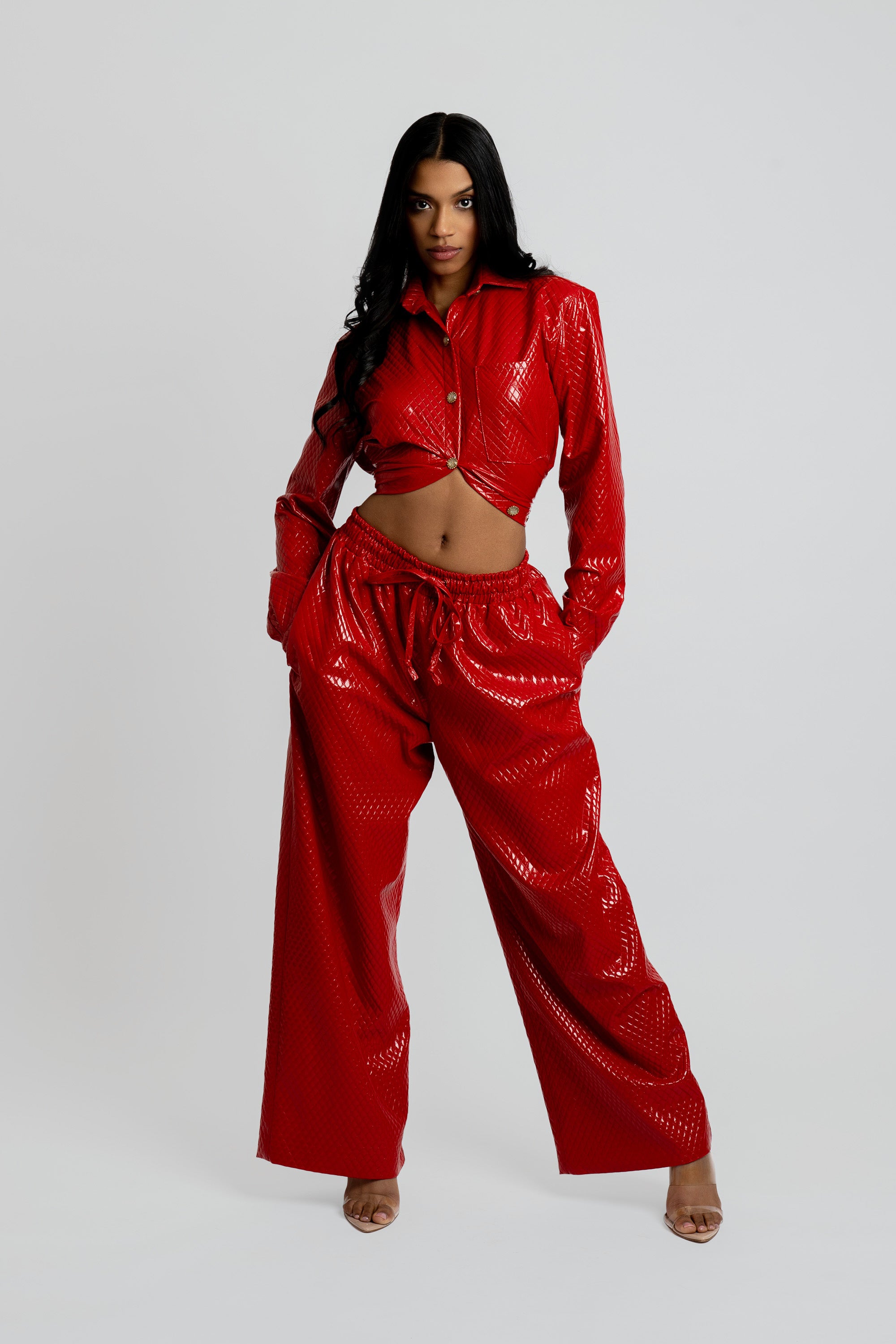 Woman wearing a red textured button up top and matching pants on a plain background