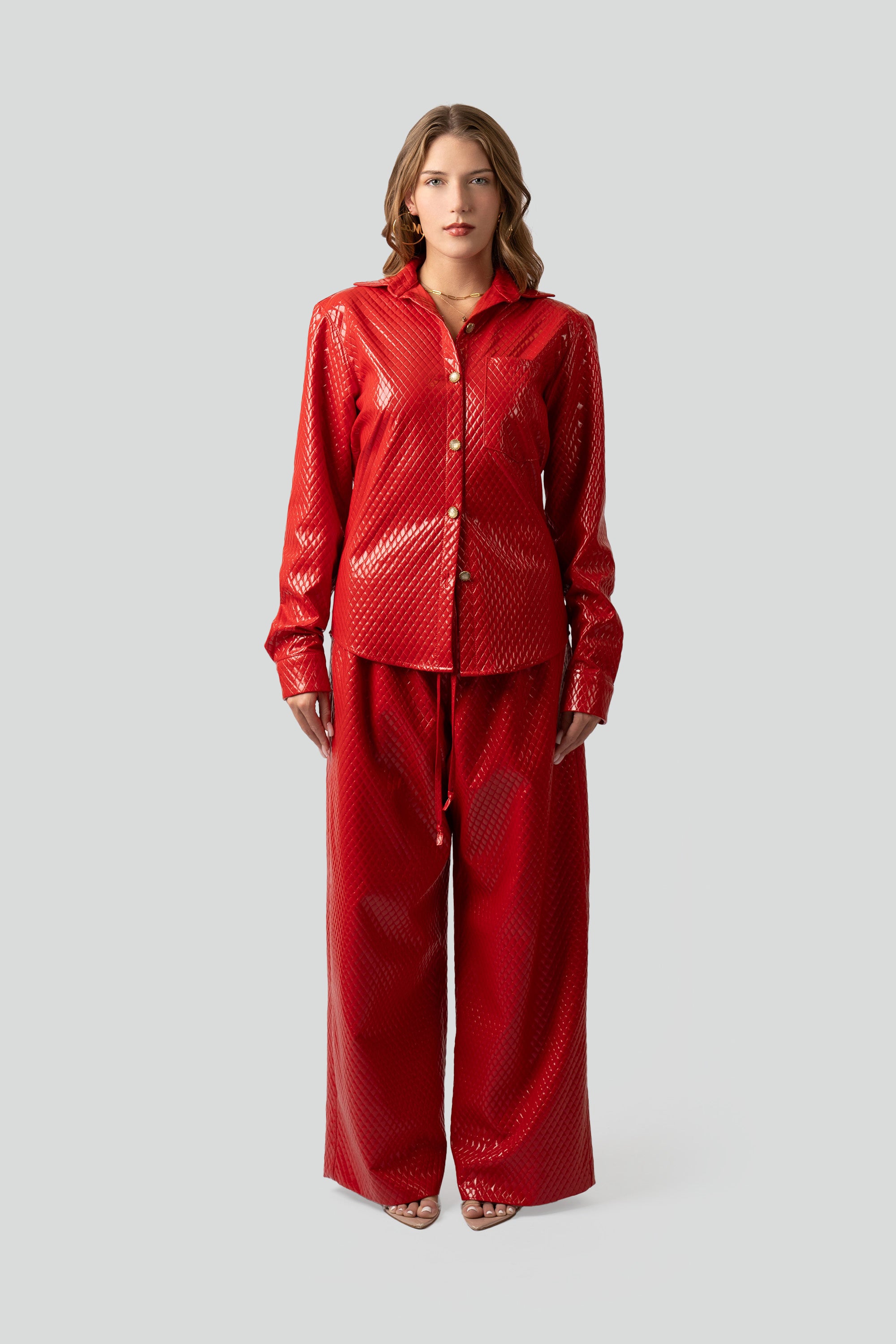 Woman wearing a red textured button up top and matching pants on a plain background