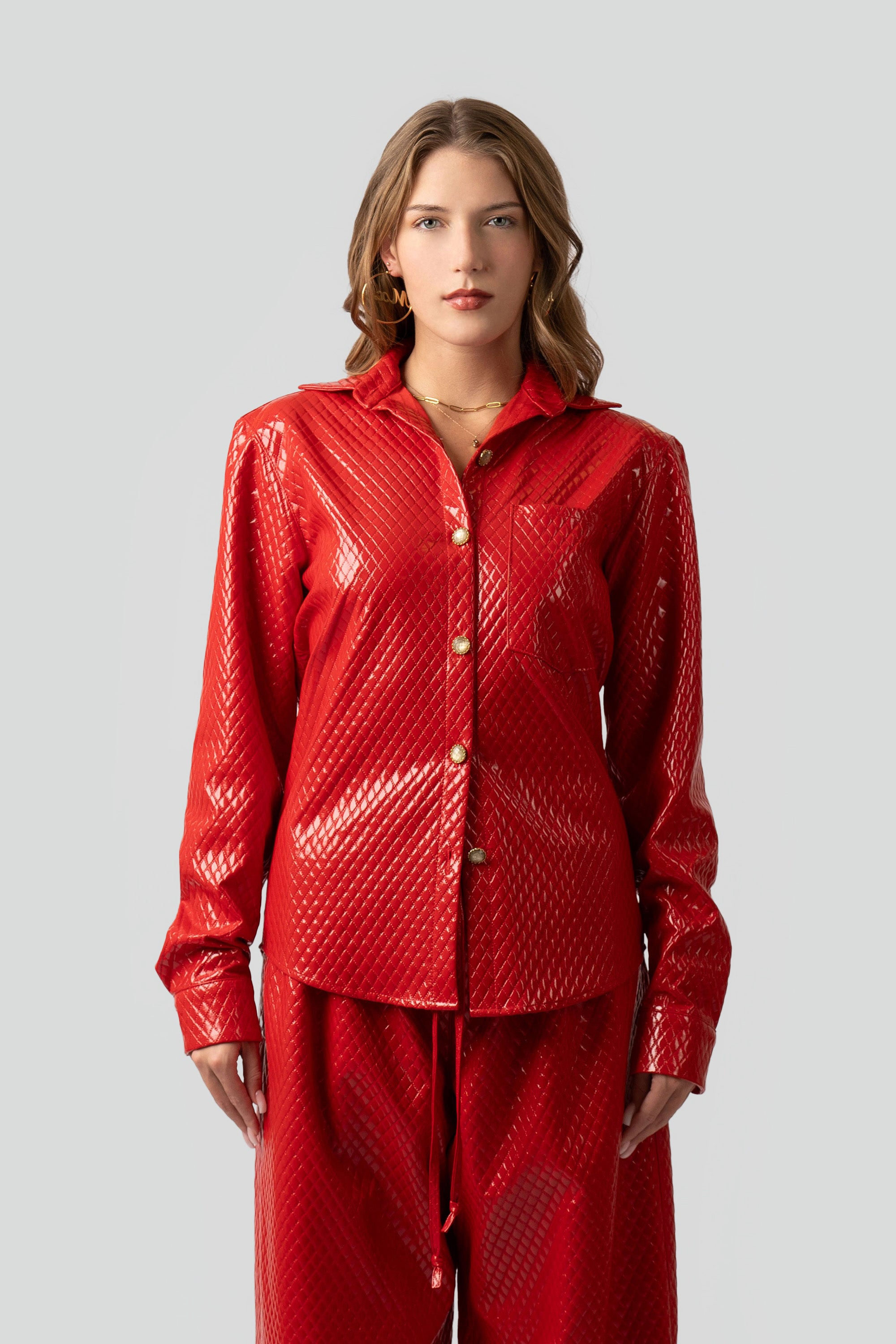 Woman wearing a red textured button up top and matching pants on a plain background