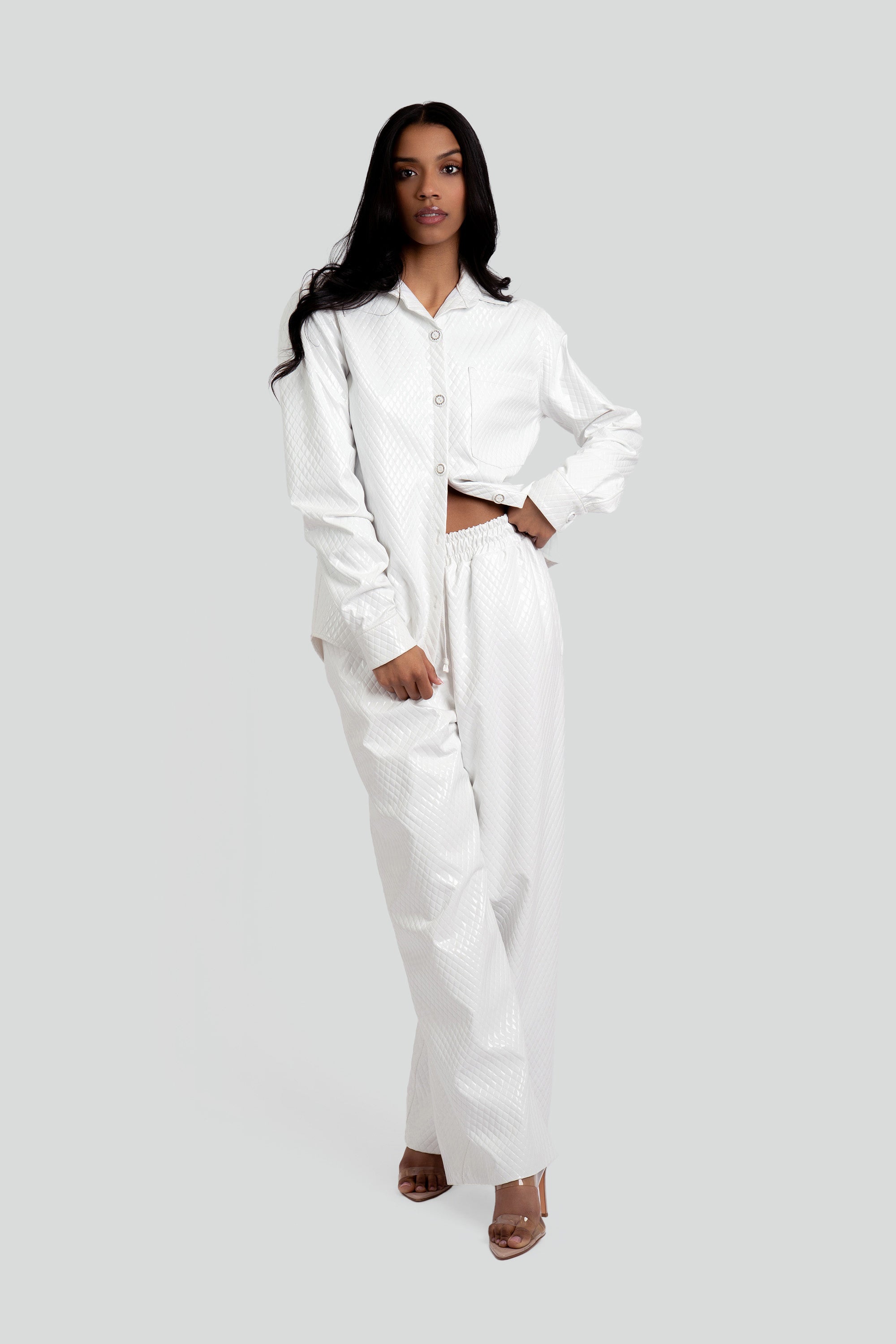 Woman wearing a white textured button up top and matching pants on a plain background