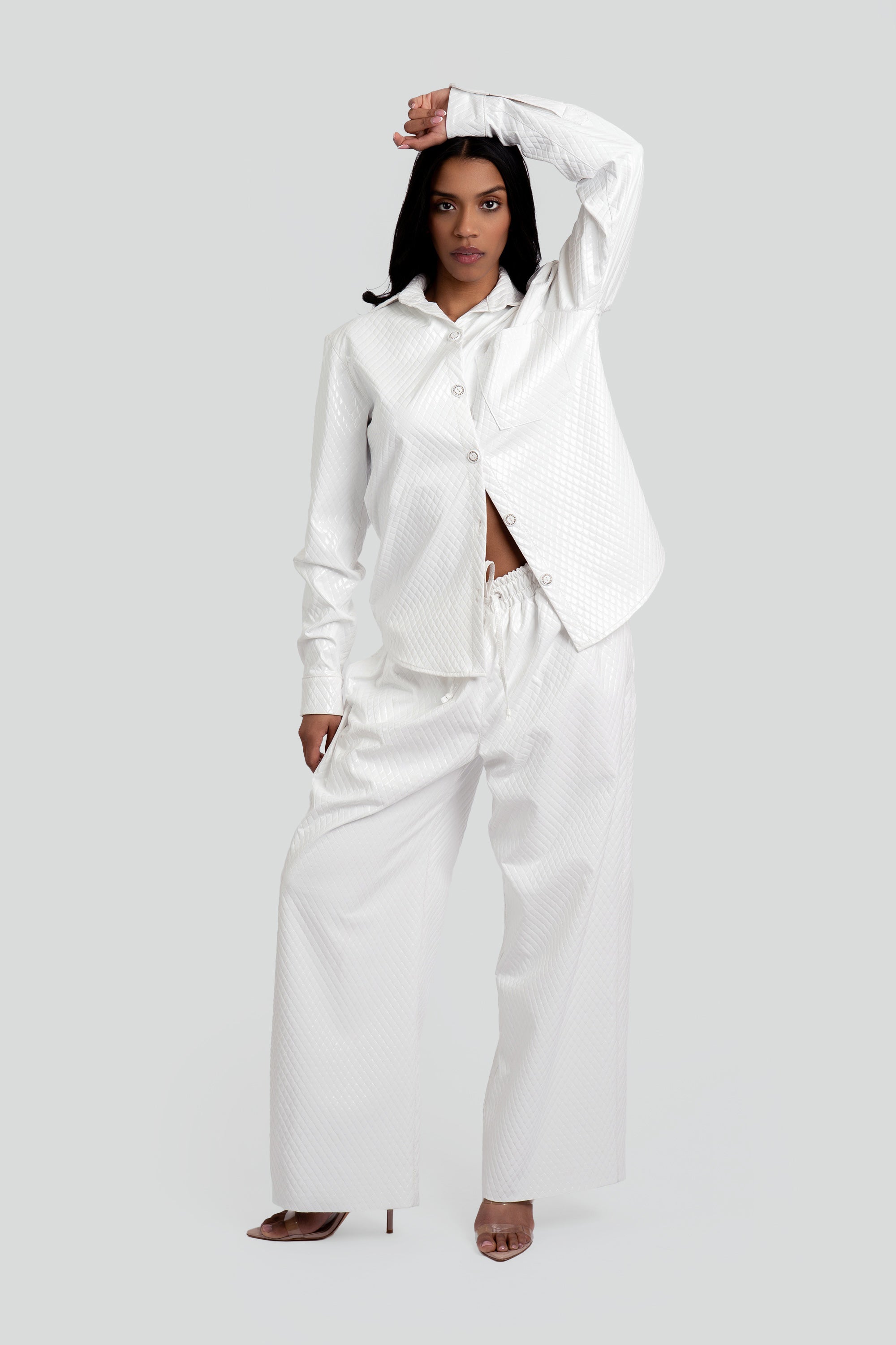Woman wearing a white textured button up top and matching pants on a plain background