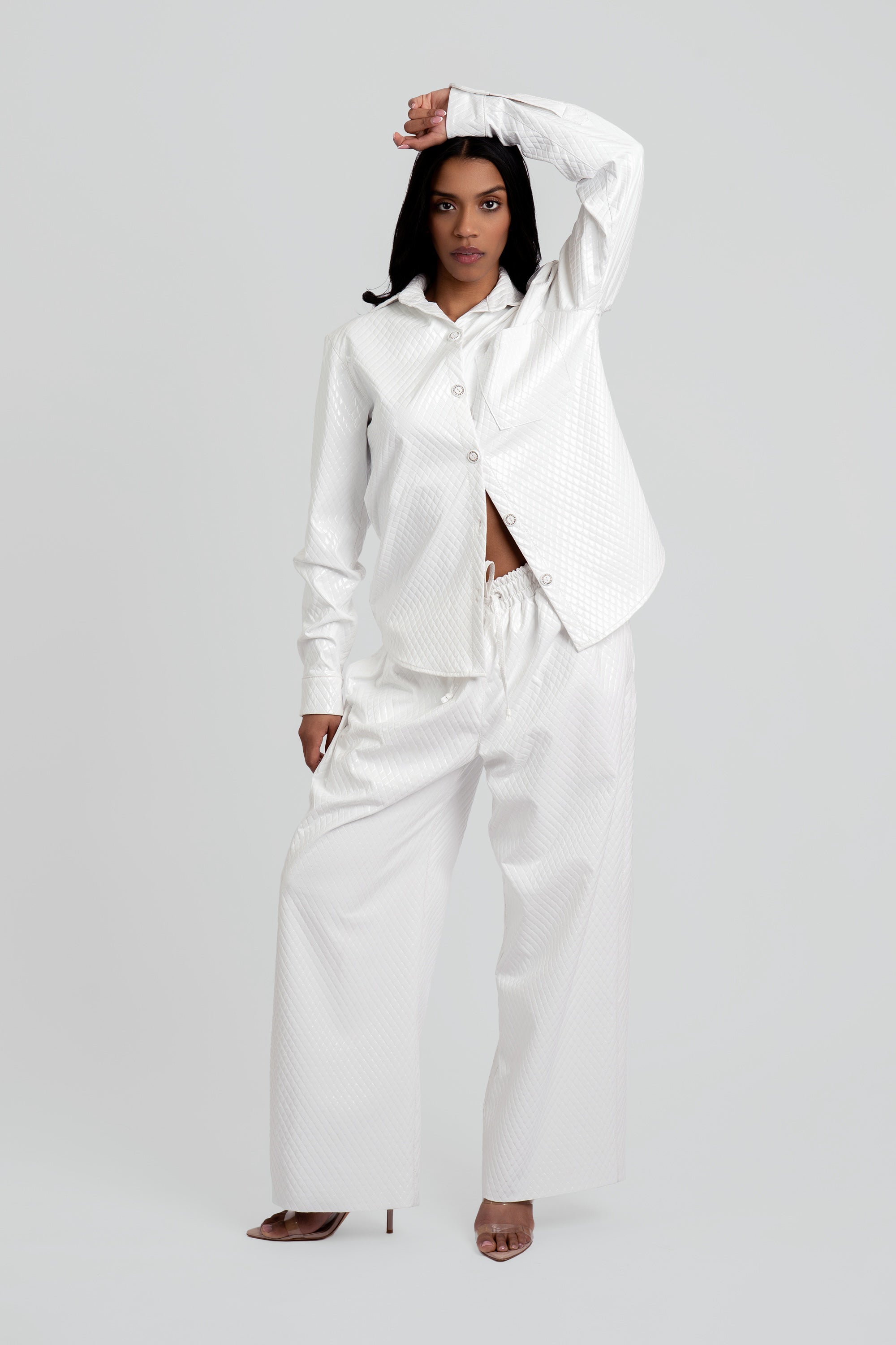 Woman wearing a white textured button up top and matching pants on a plain background