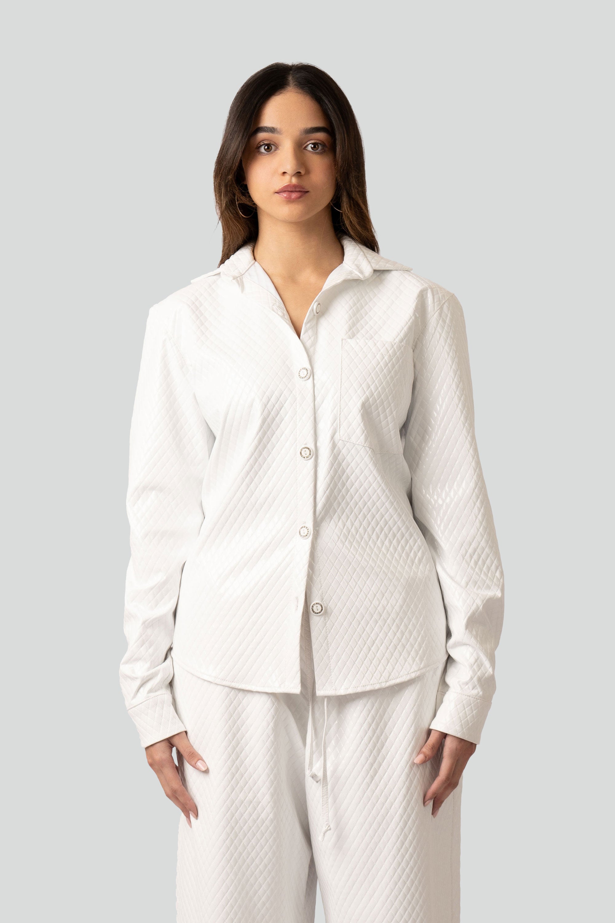 Woman wearing a white textured button up top and matching pants on a plain background
