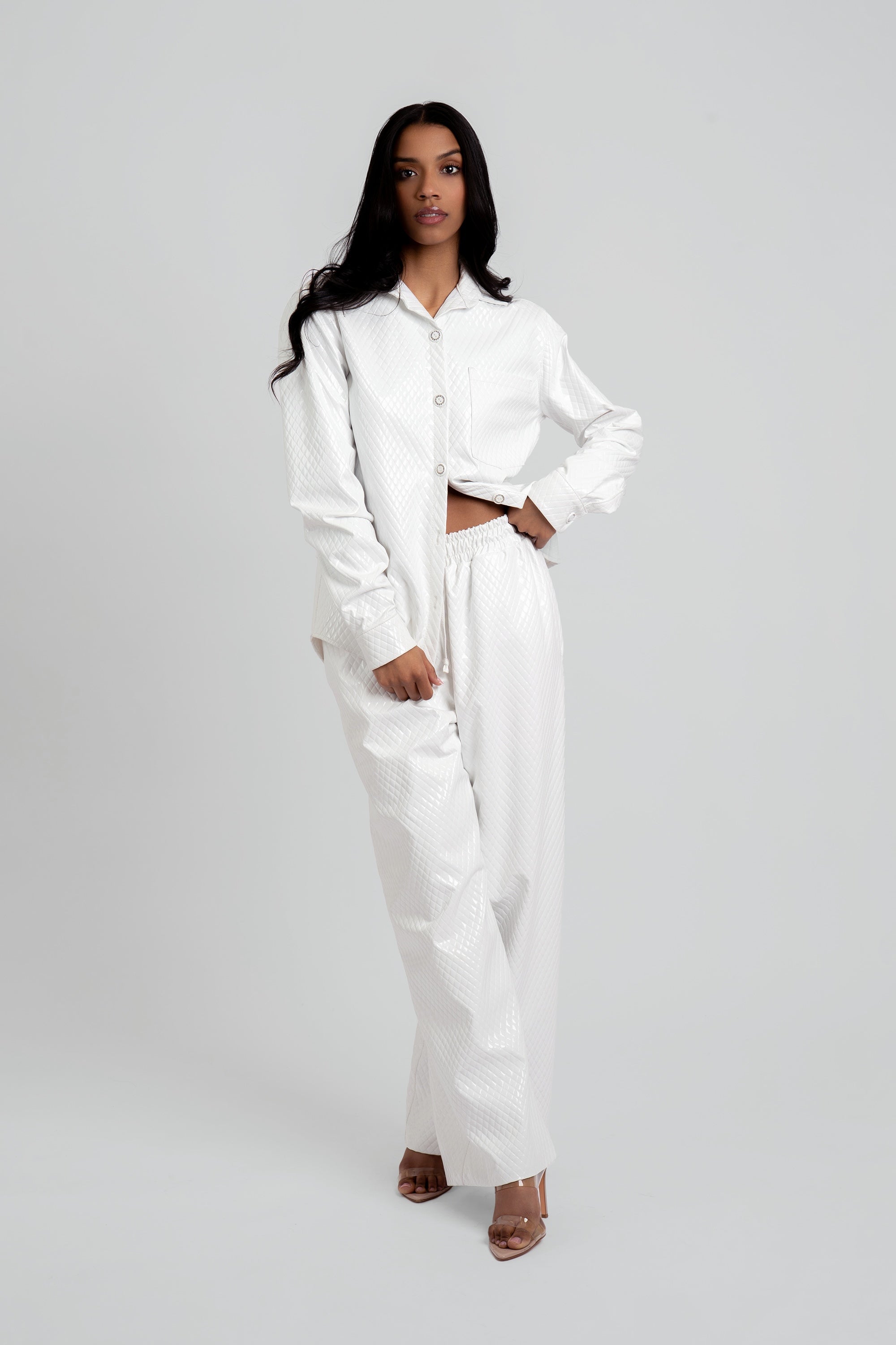 Woman wearing a white textured button up top and matching pants on a plain background