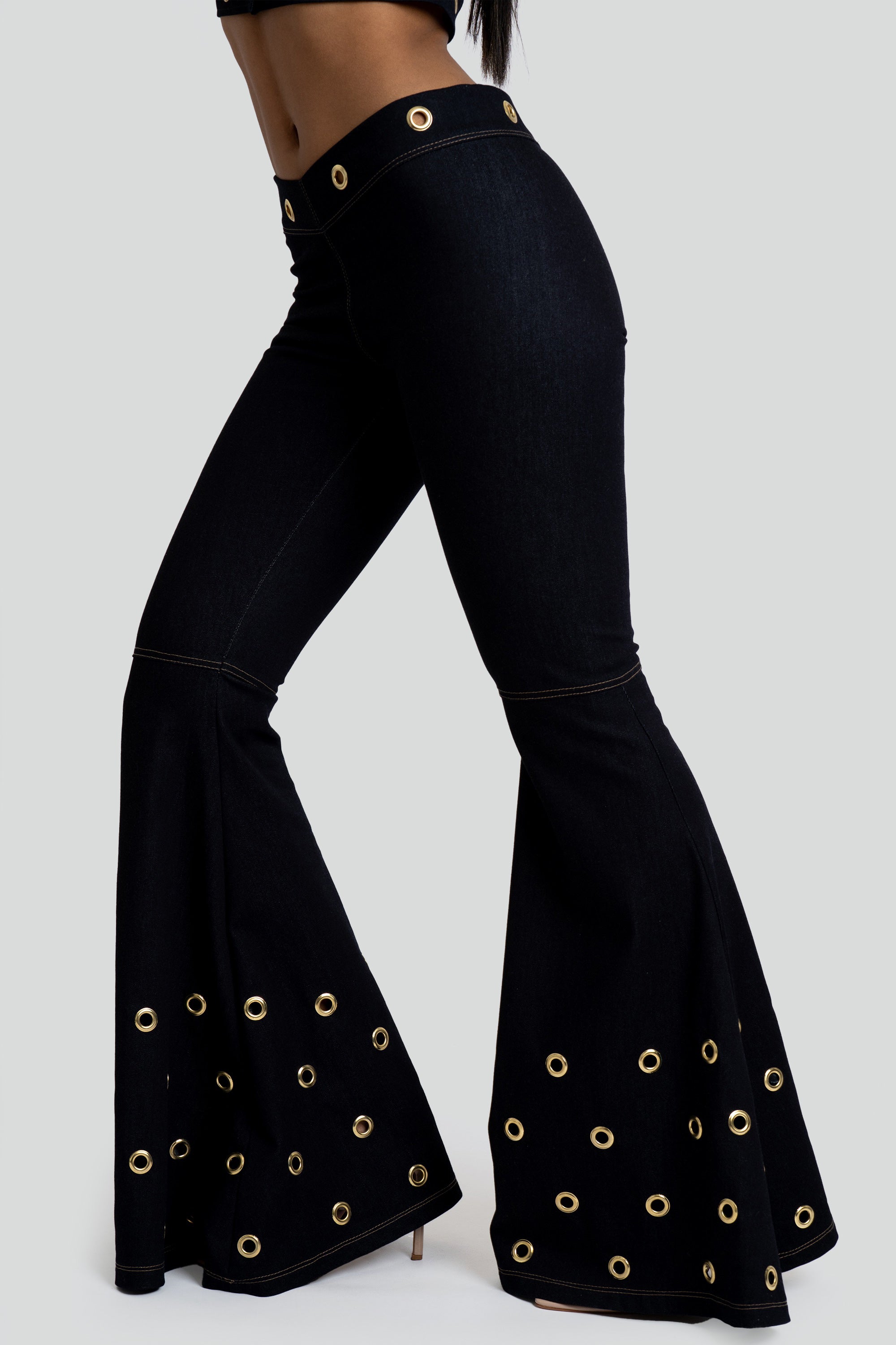 Dark denim bell-bottom pants with gold grommet details on a white background