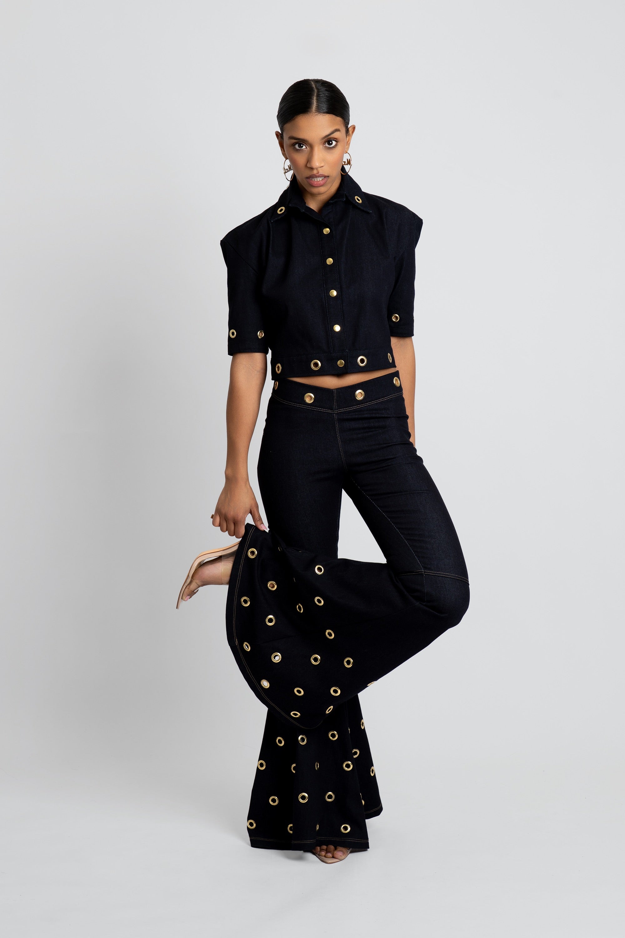 Woman wearing a dark denim outfit with gold embellishments on a white background