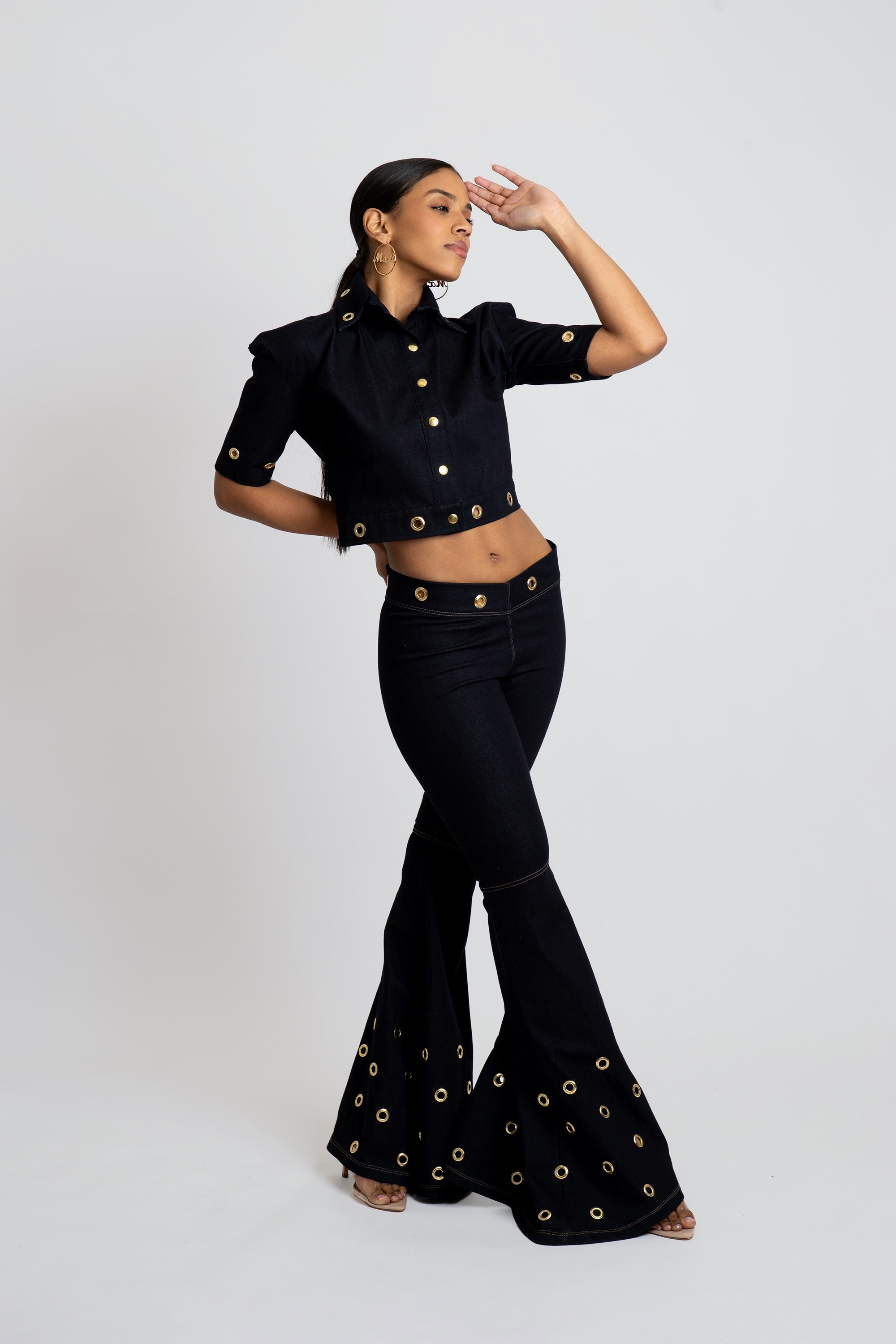 Woman wearing a dark denim outfit with gold embellishments on a white background