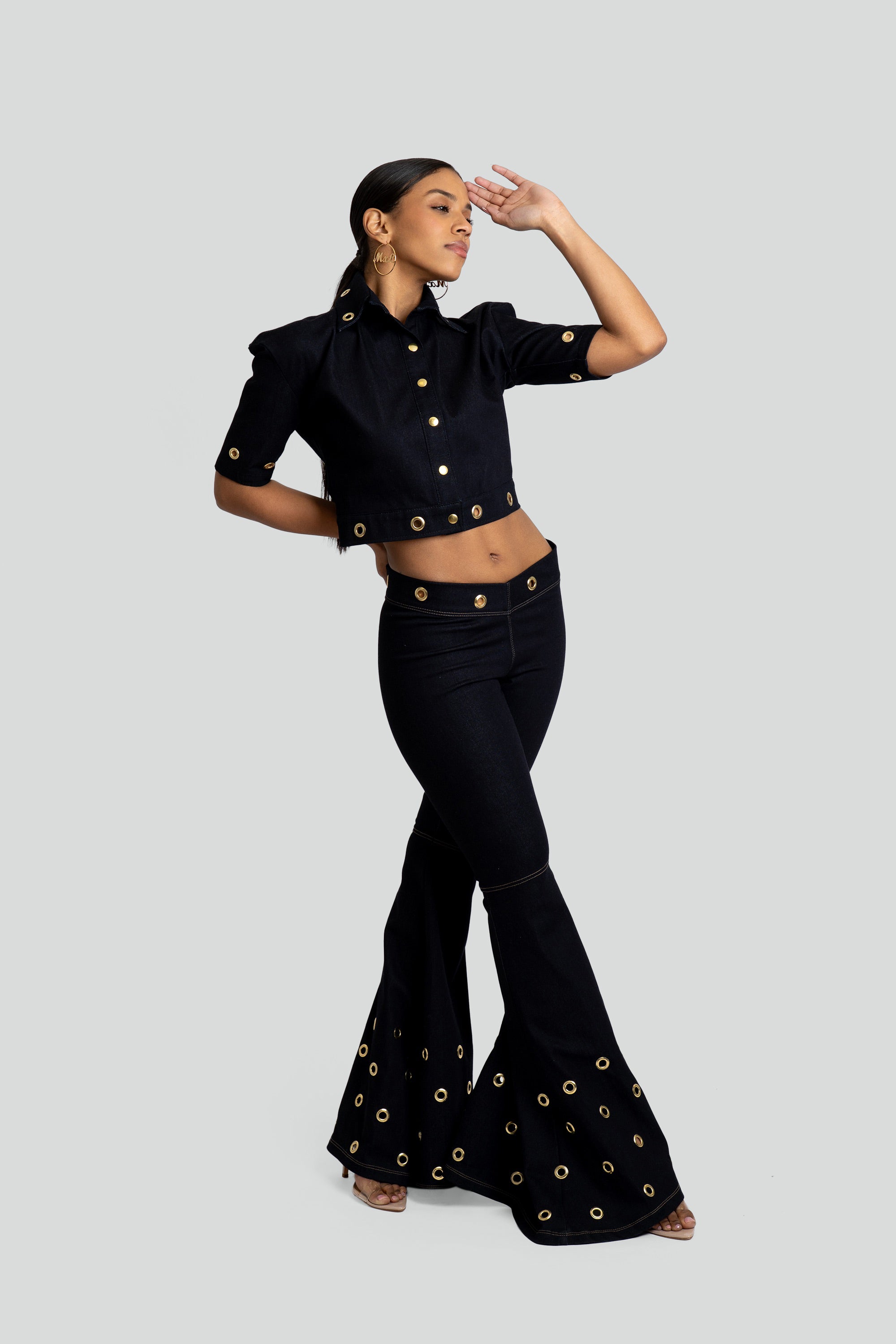 Woman wearing a dark denim outfit with gold embellishments on a white background