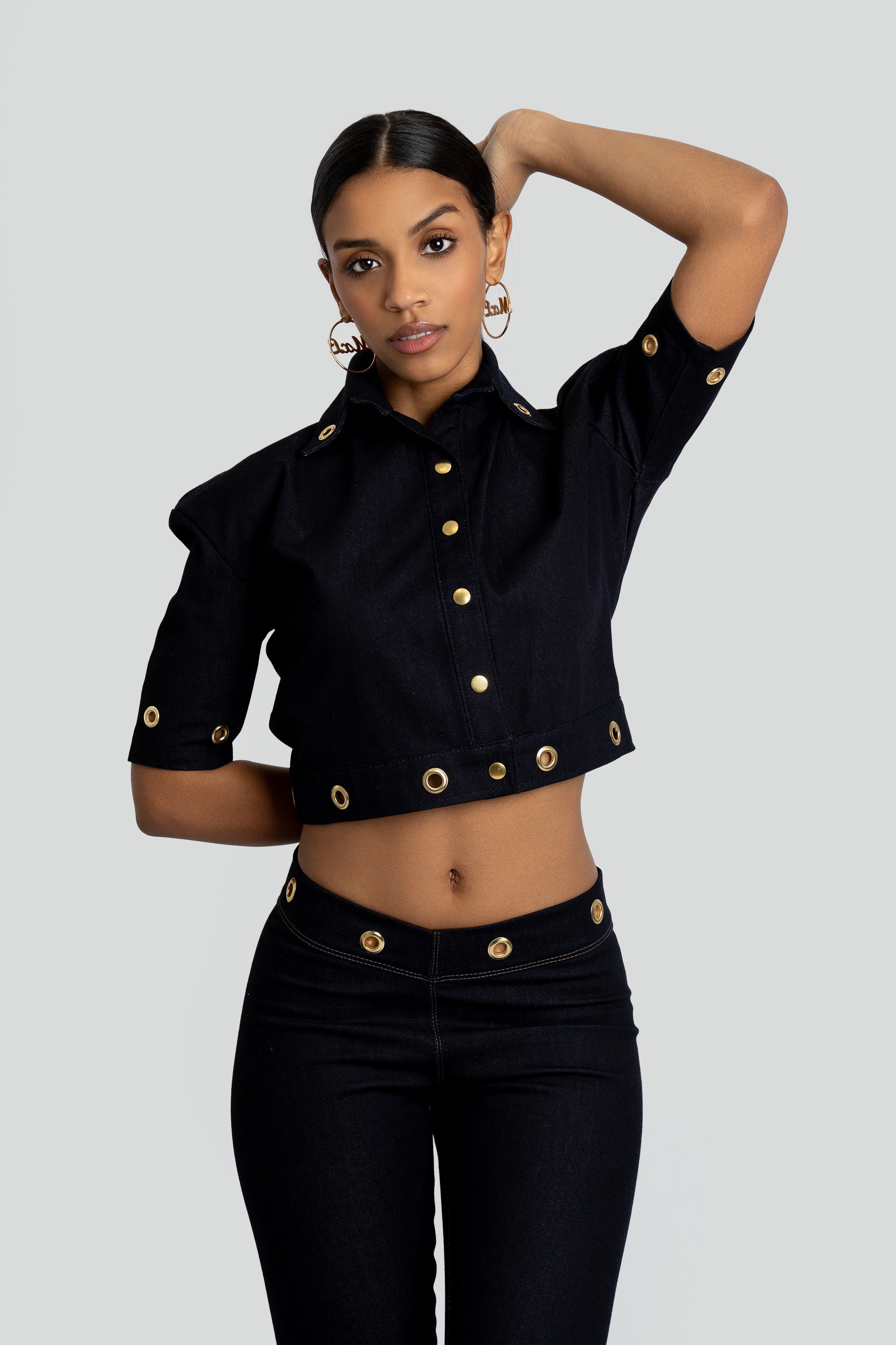 Woman wearing a dark denim outfit with gold embellishments on a plain background