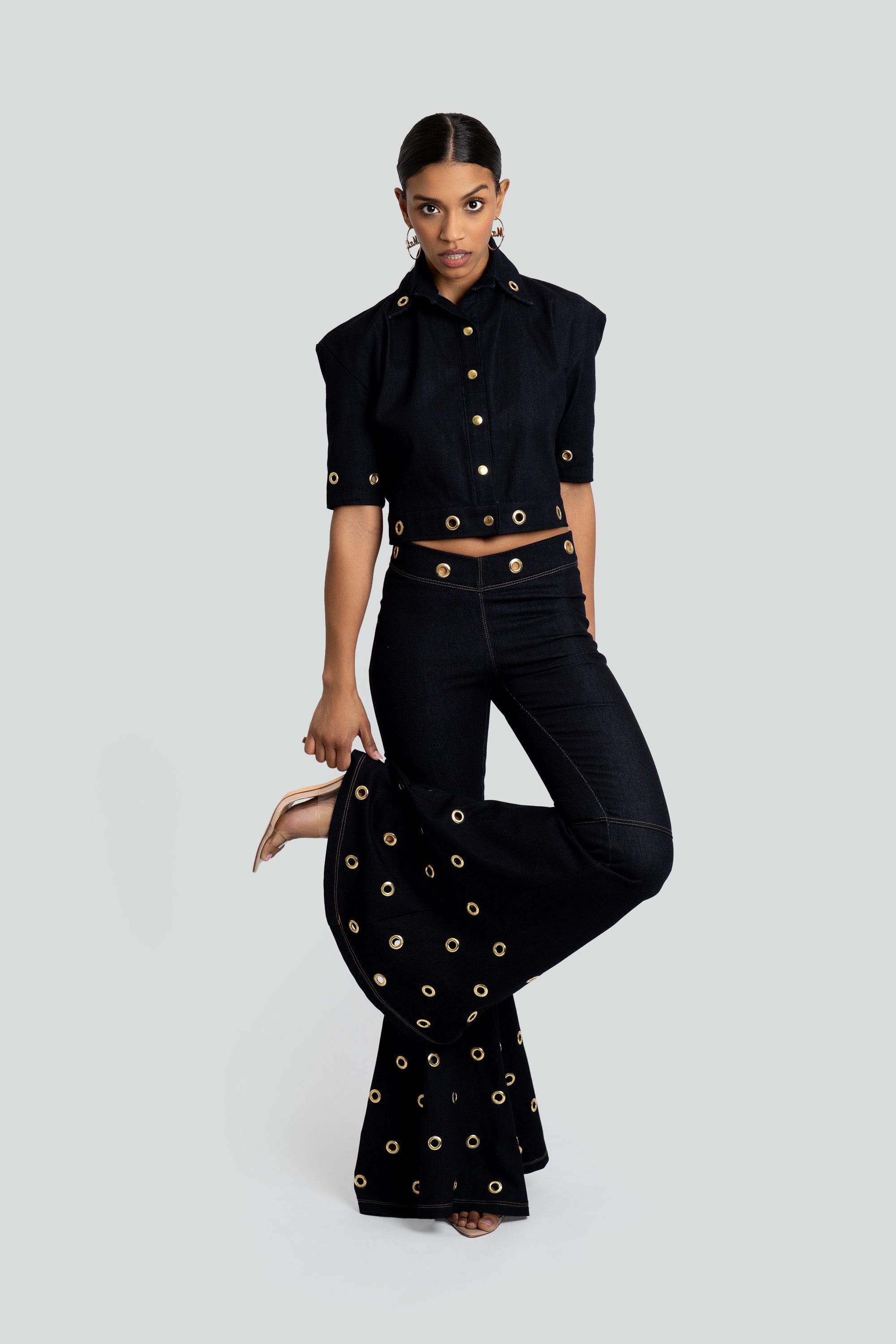 Woman wearing a dark denim outfit with gold embellishments on a white background