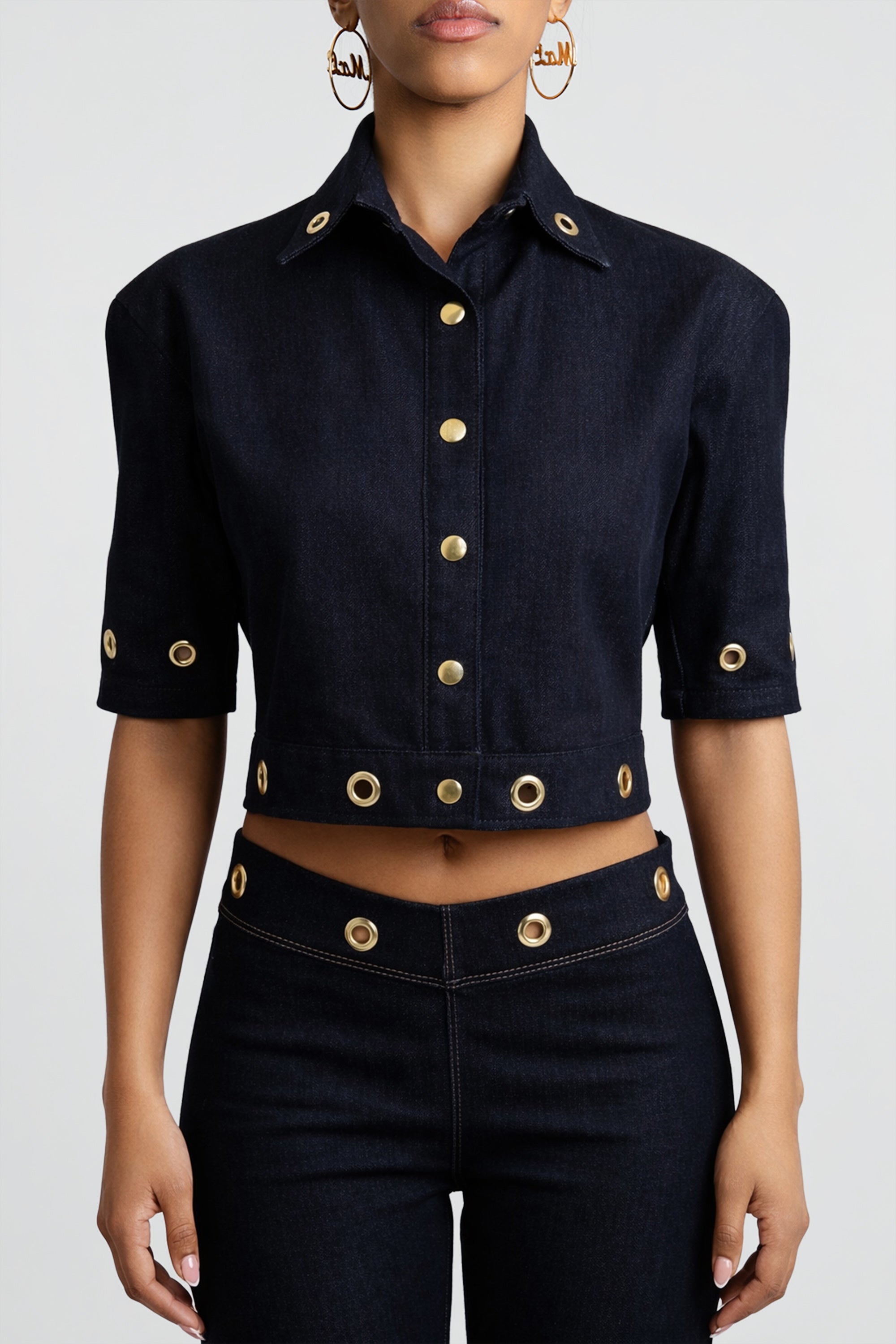 Cropped dark denim shirt with gold embellishments worn by a person on a gray background