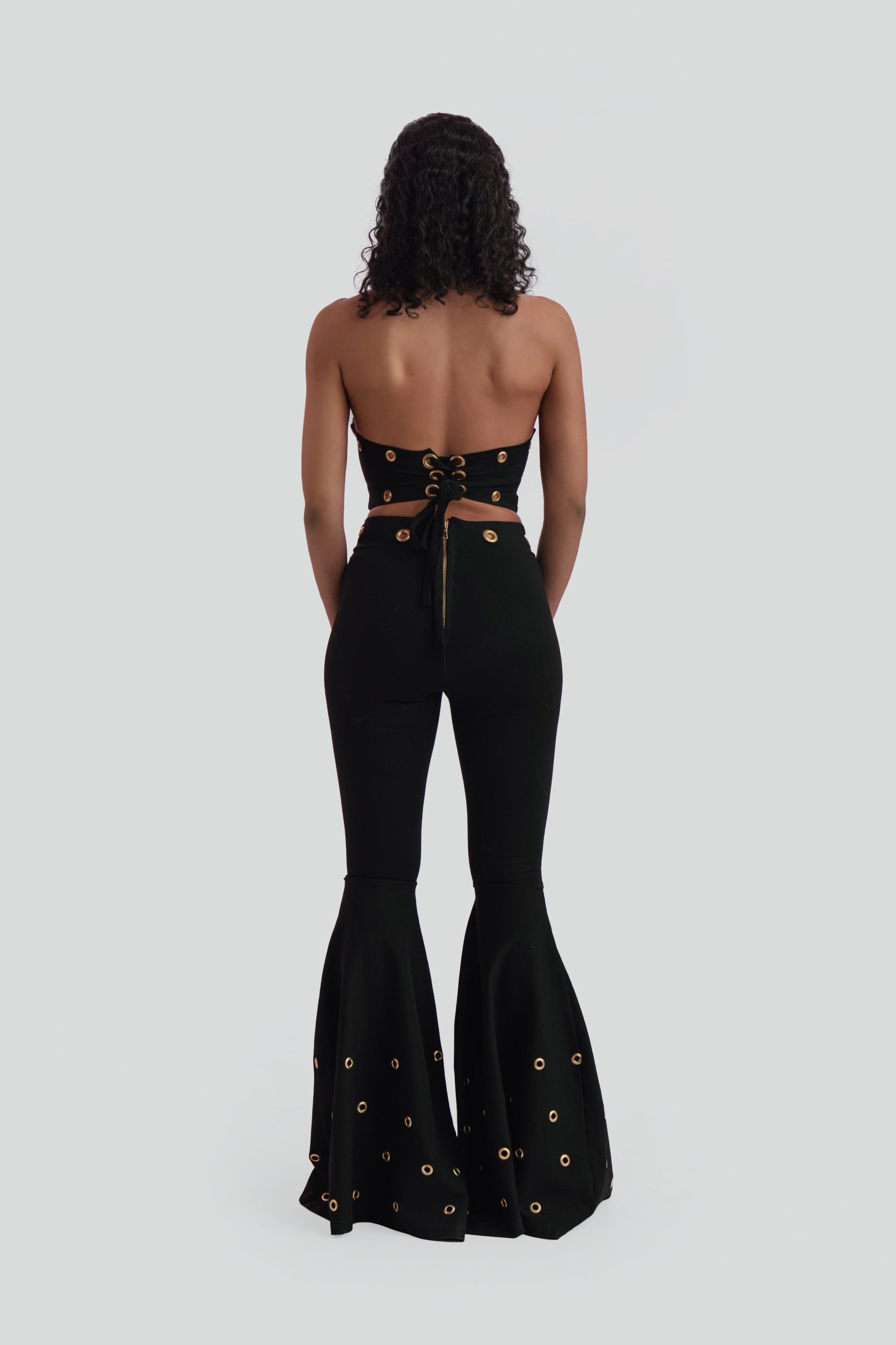 Black outfit with open back and gold embellishments on a white background