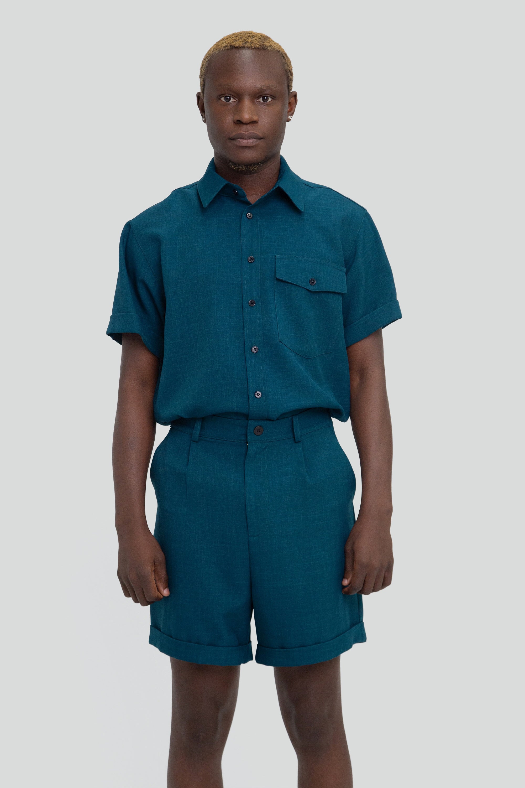 Person wearing a dark teal shirt and shorts set on a plain background