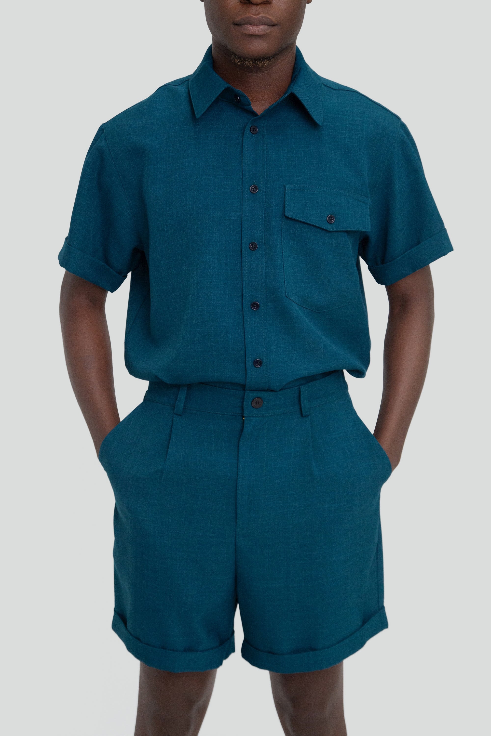 Person wearing a dark teal shirt and shorts set on a plain background