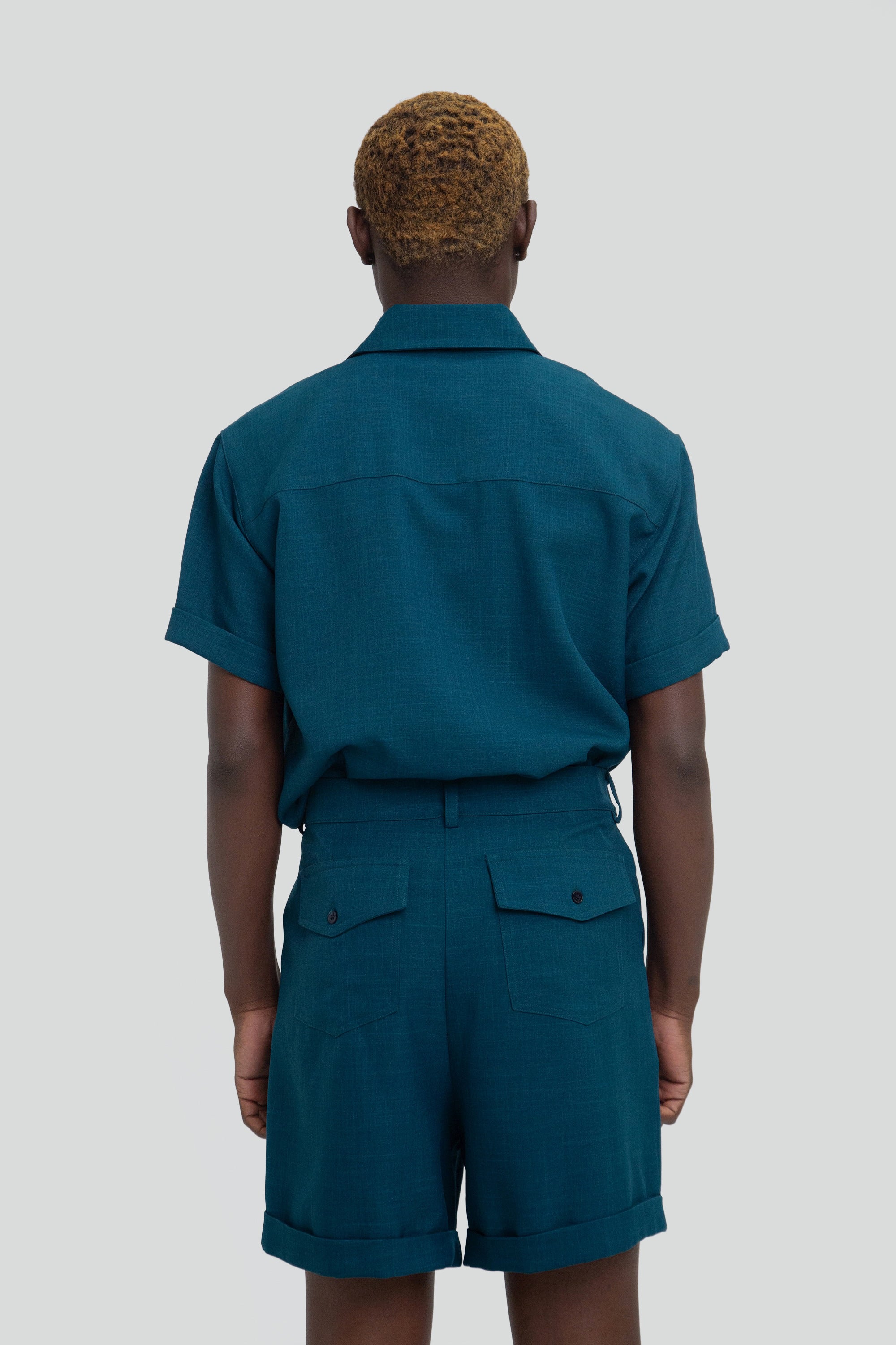 Person wearing a dark teal shirt and shorts set on a plain background