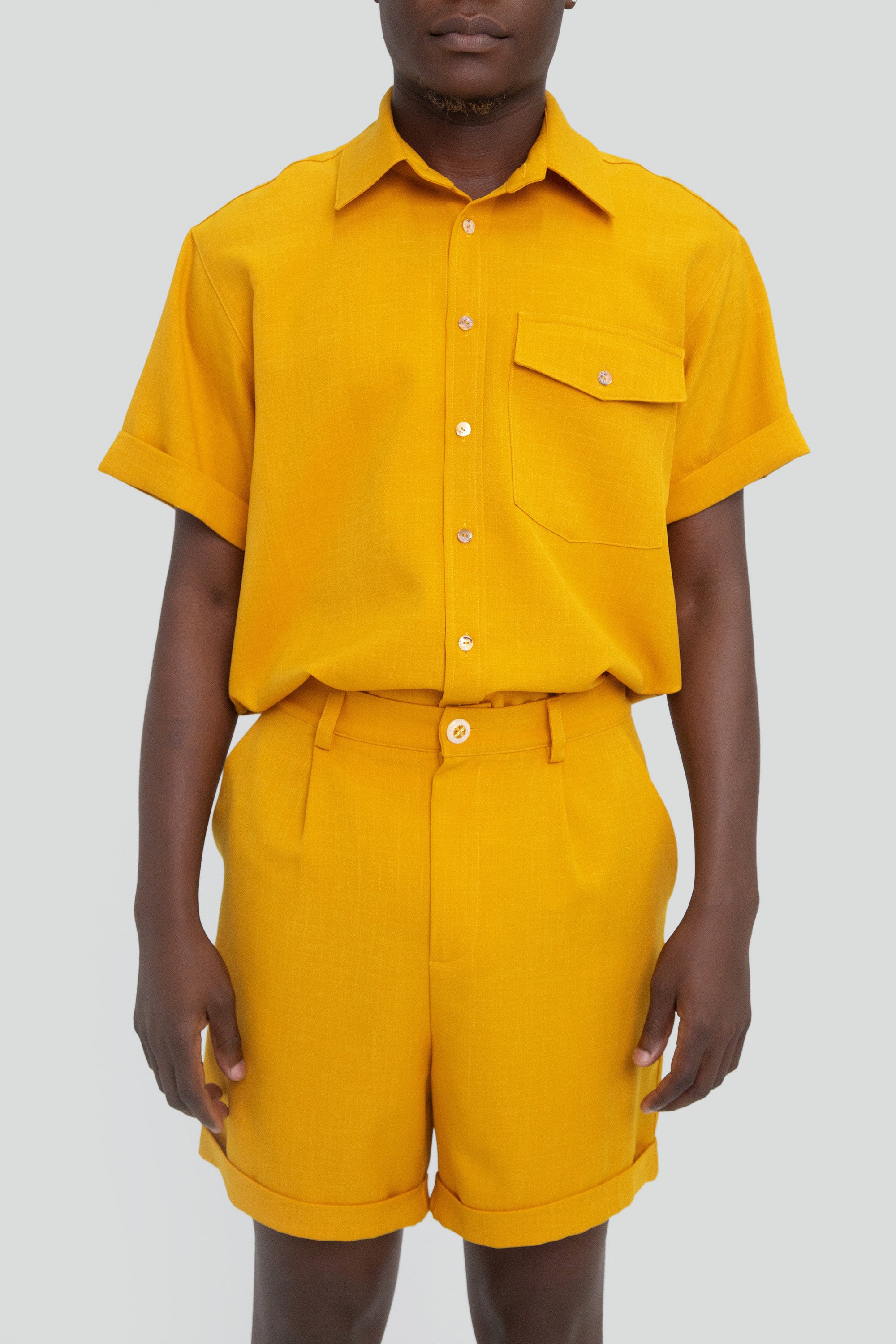 Person wearing a mustard yellow shirt and shorts set on a plain background