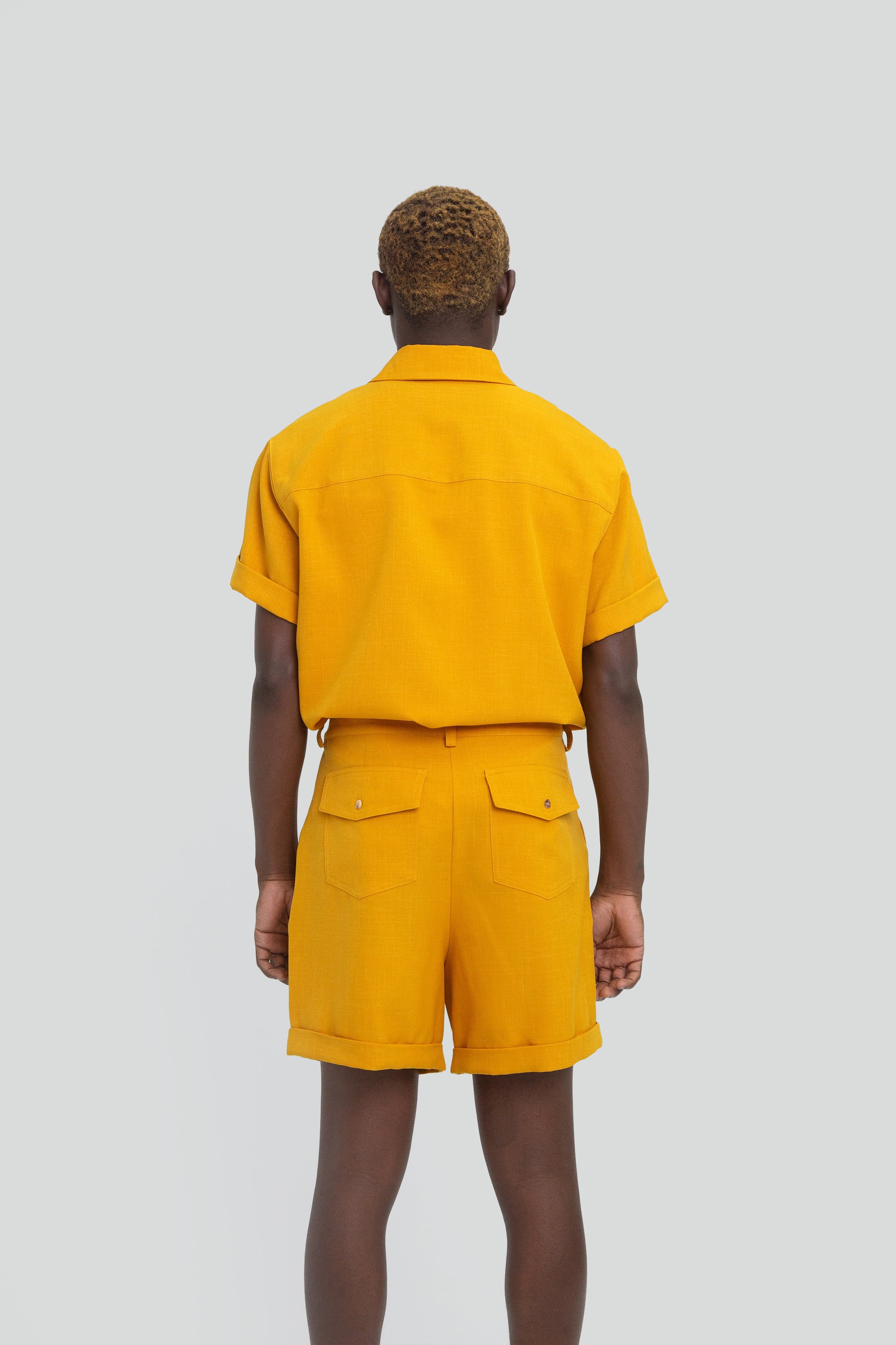 Person wearing a mustard yellow shirt and shorts set on a plain background