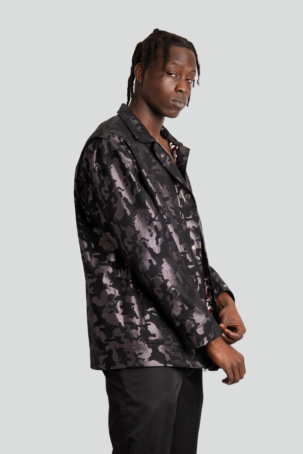 Man wearing a metallic black camouflage denim utility jacket featuring an oversized fit and five silver button front closures