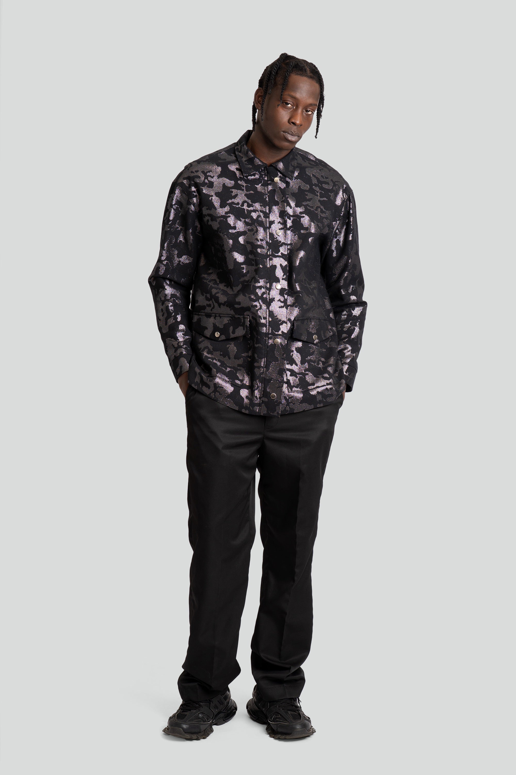 Person wearing a dark camouflage shirt and black pants on a white background