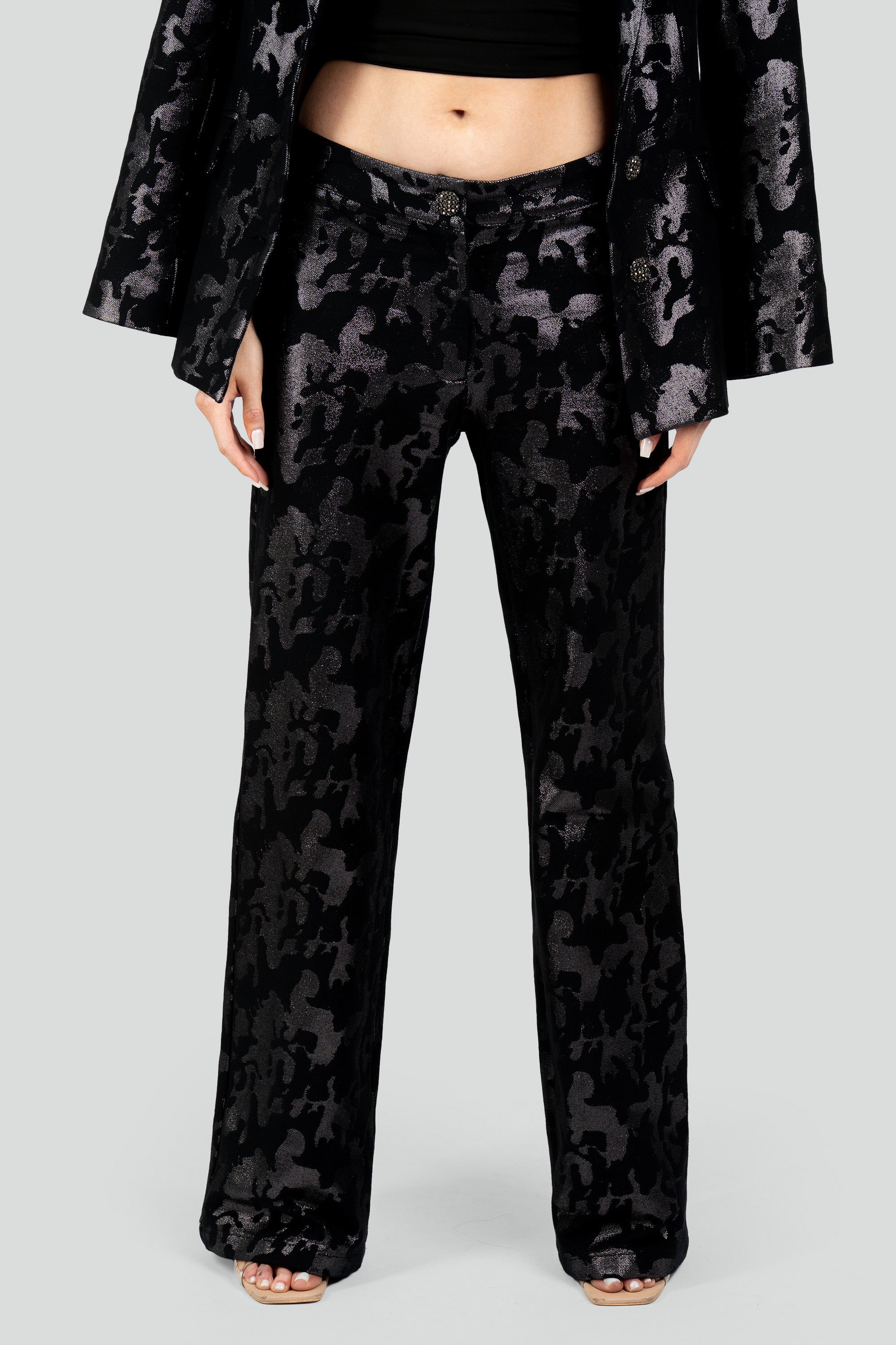Close up view of a woman wearing black camo suit pants on a white background