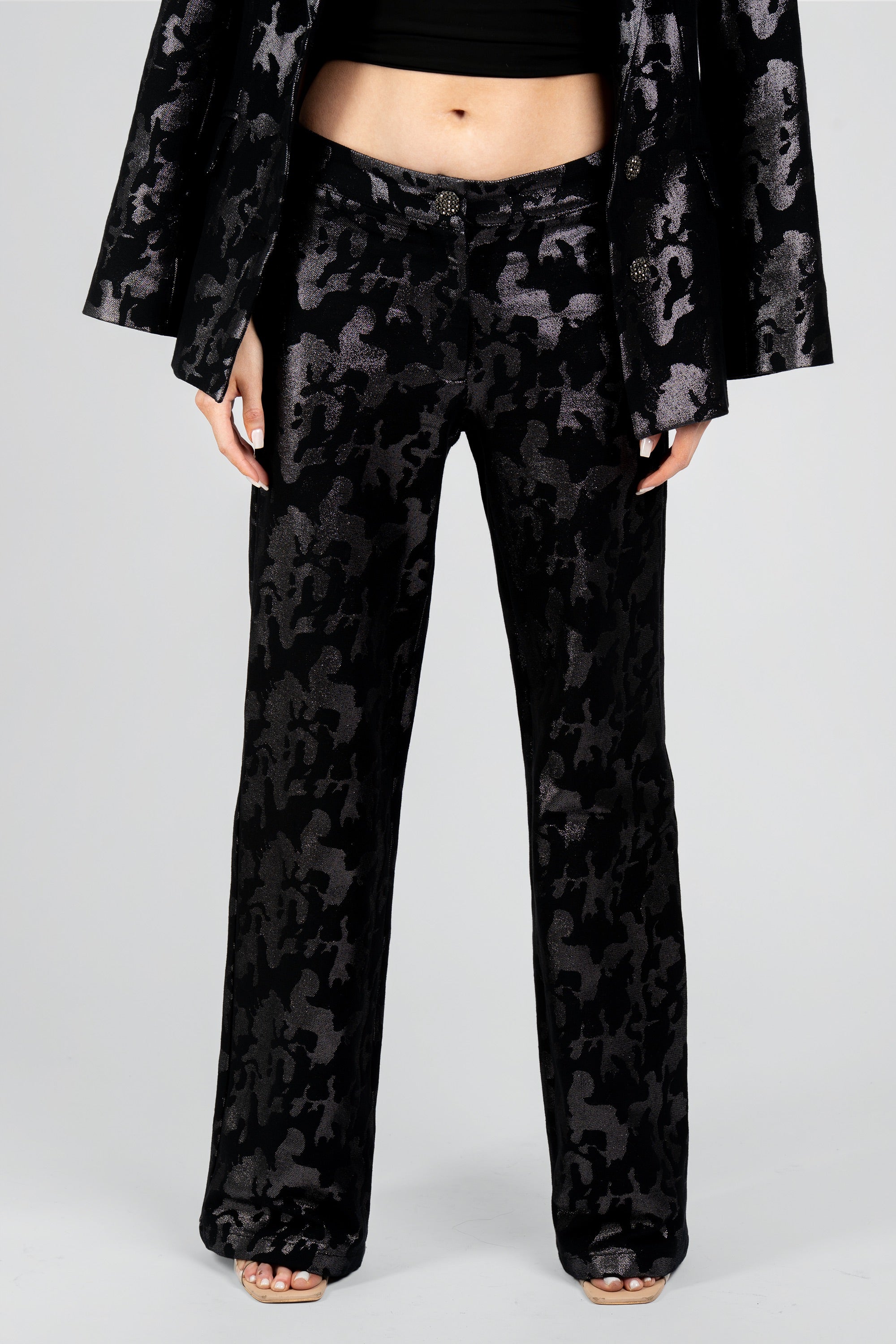 Close up view of a woman wearing black camo suit pants on a white background