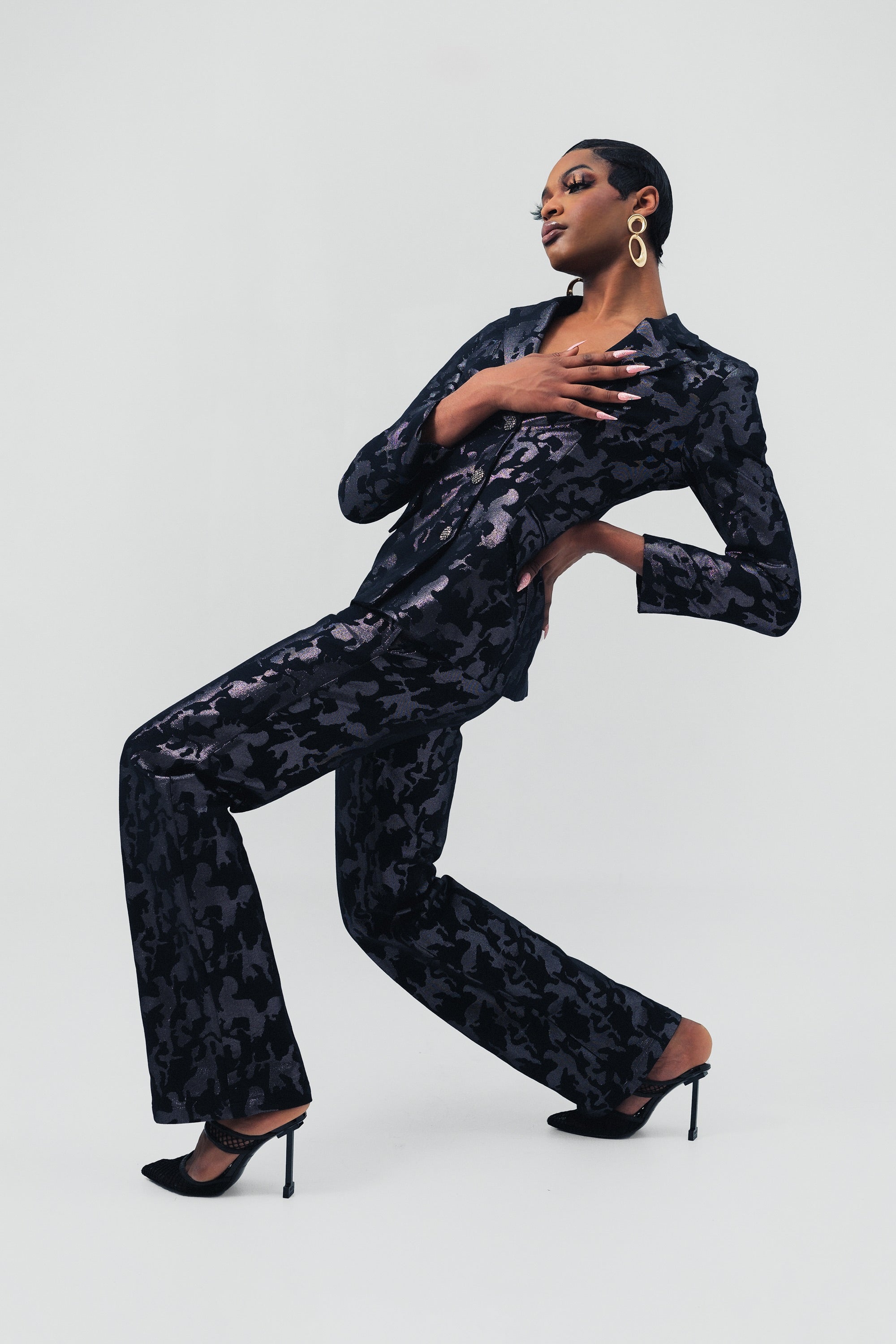 Woman wearing a black camo suit set dramatically posing on a white background