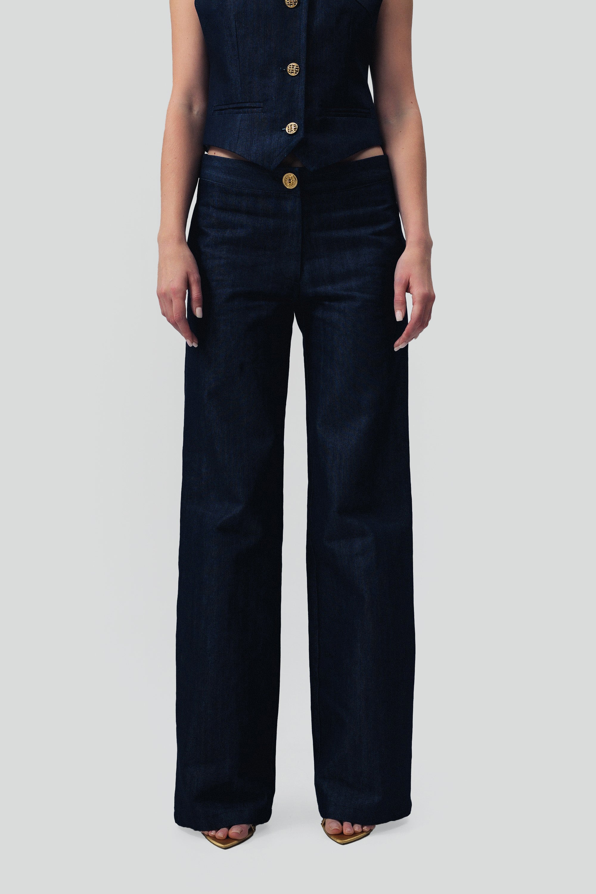 Close up view of a woman wearing dark blue denim pants with gold buttons on a grey background