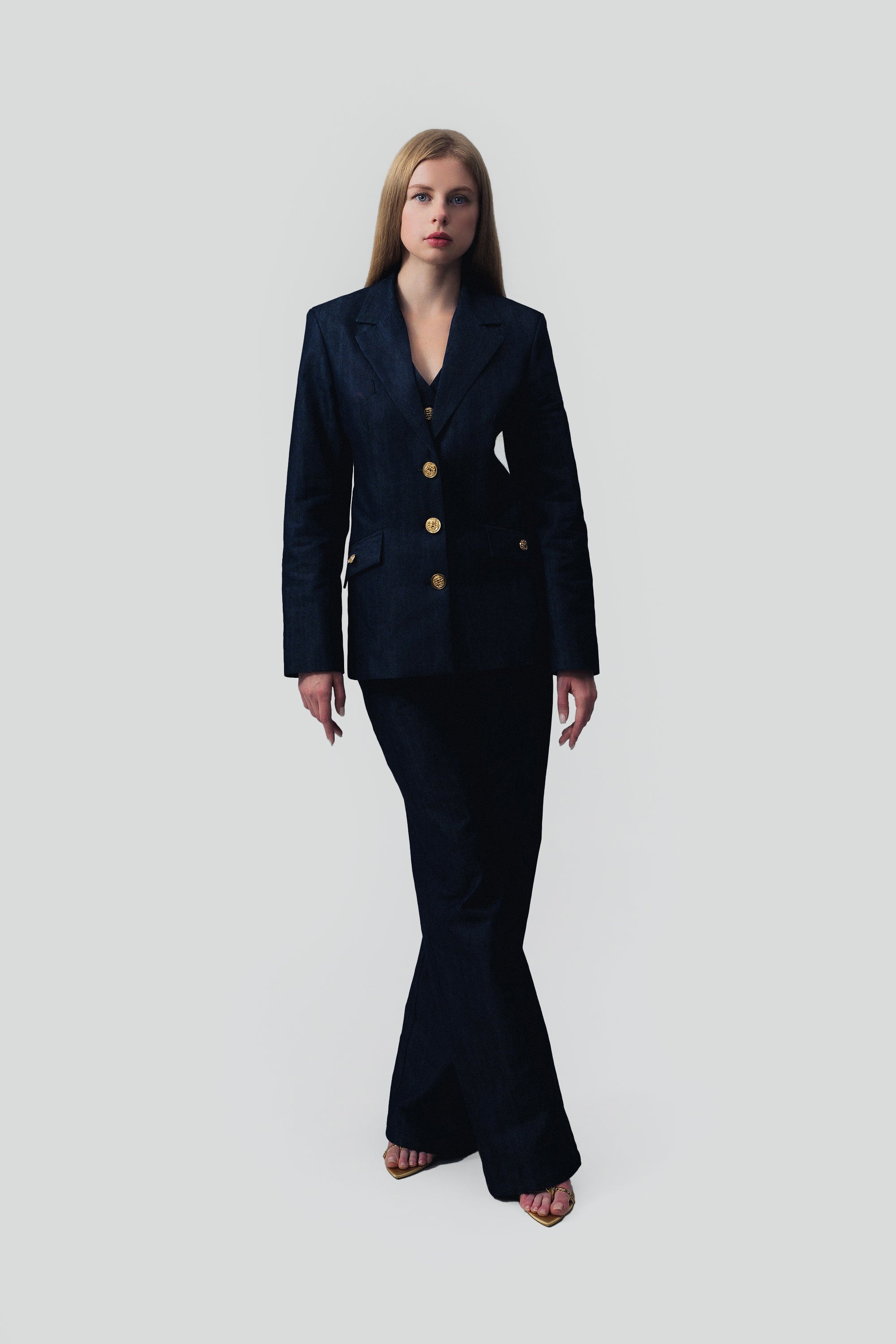 Woman wearing a dark blue denim suit with gold buttons on a gray background