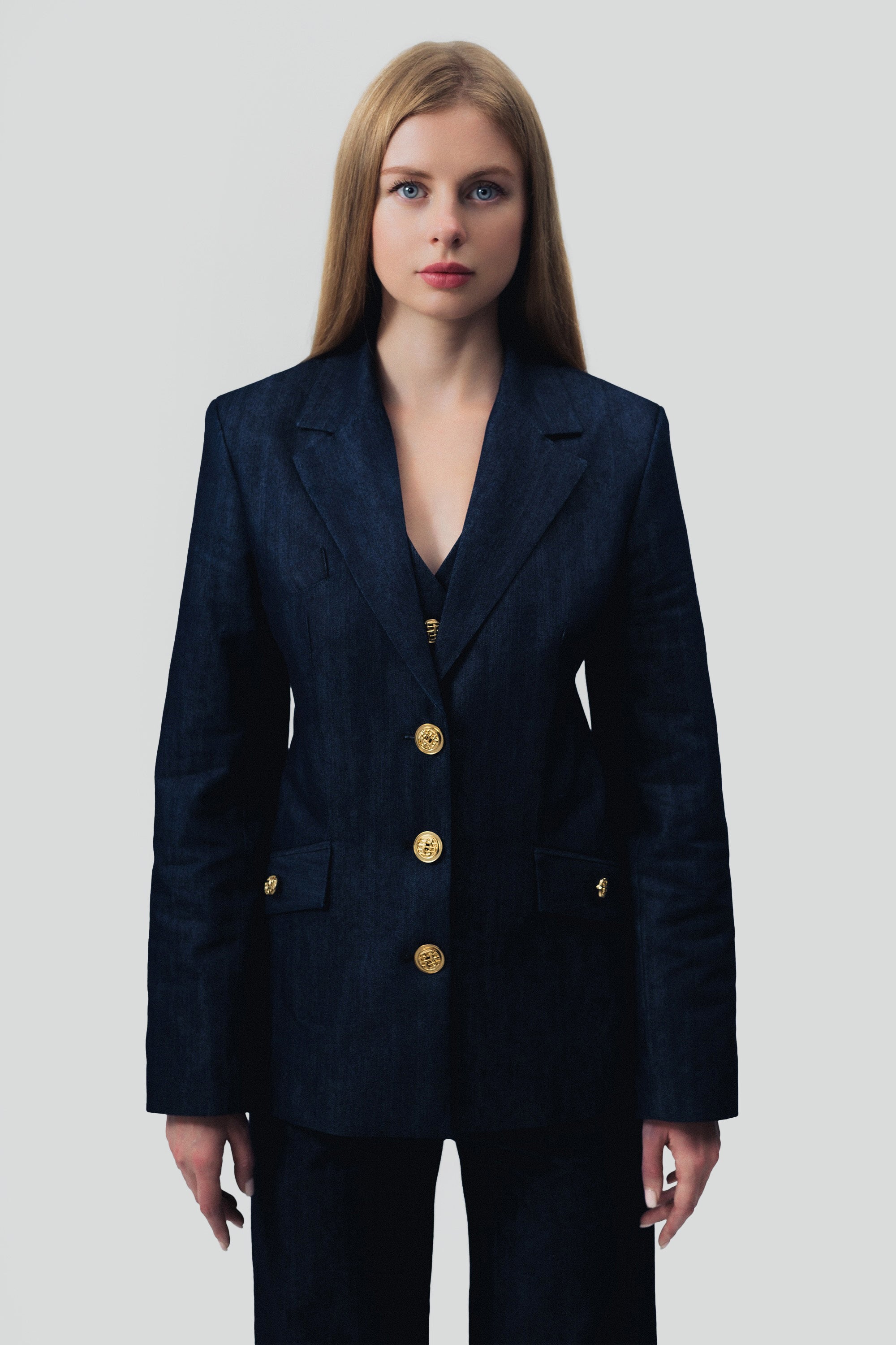 Woman wearing a dark blue denim suit with gold buttons on a gray background