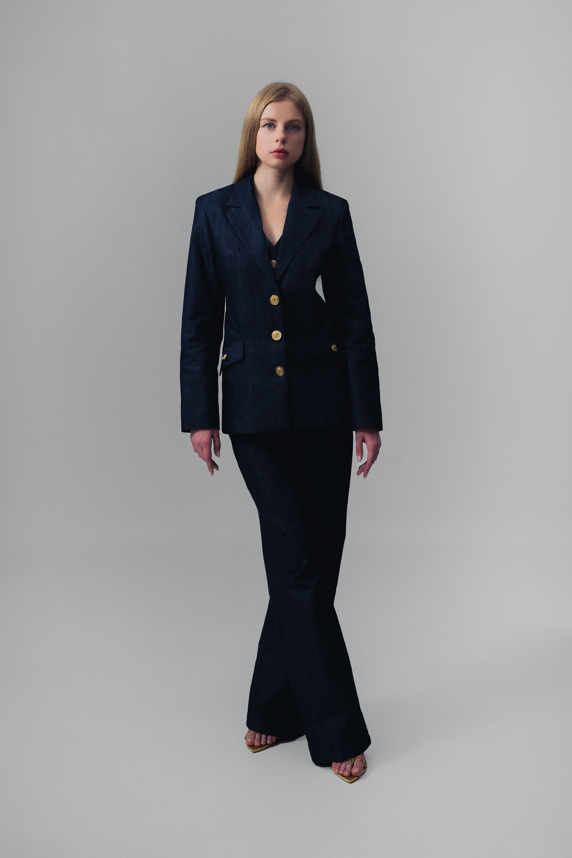 Woman wearing a dark blue denim suit with gold buttons on a gray background