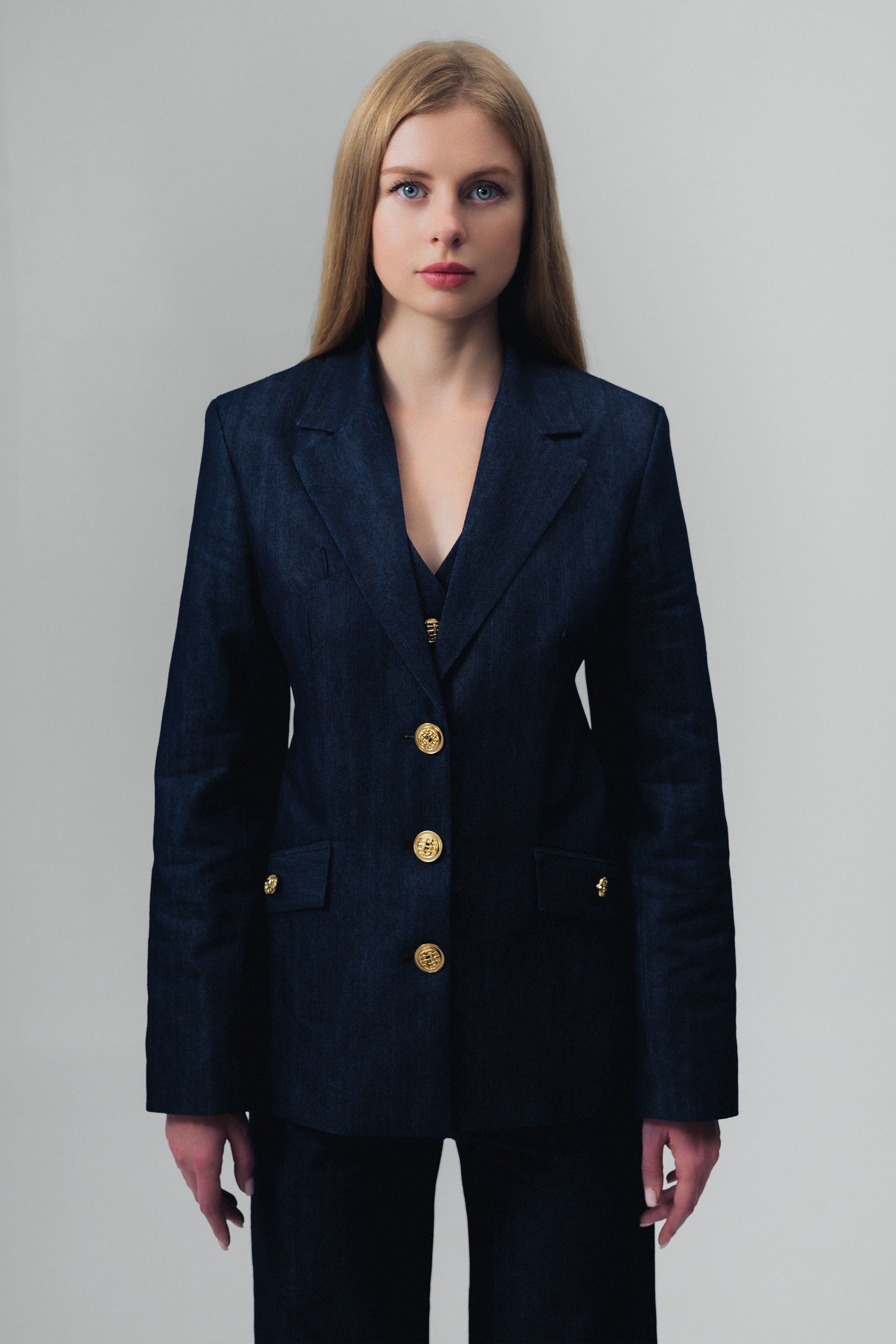 Woman wearing a dark blue denim suit with gold buttons on a gray background