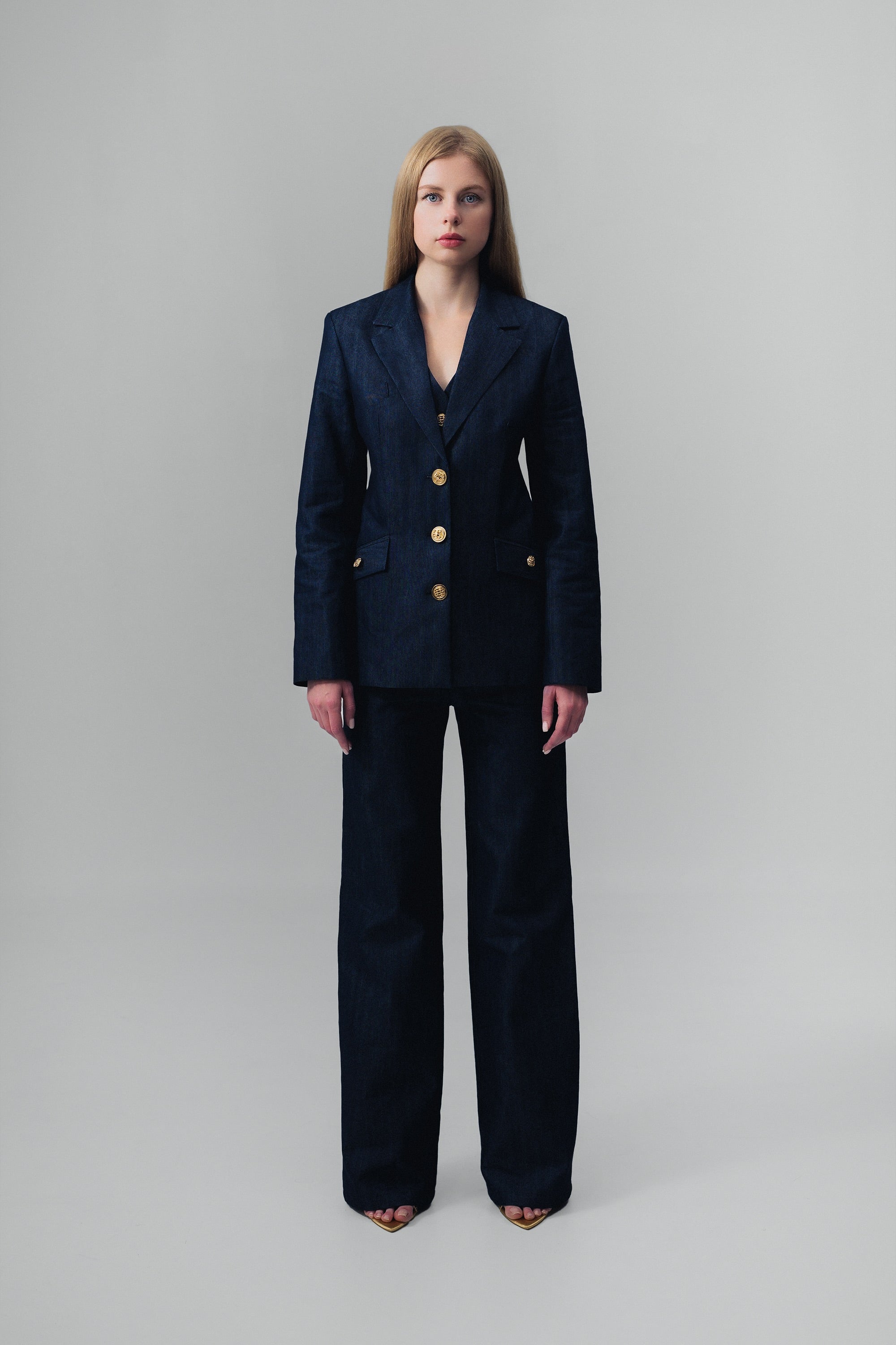 Woman wearing a dark blue denim suit with gold buttons on a gray background