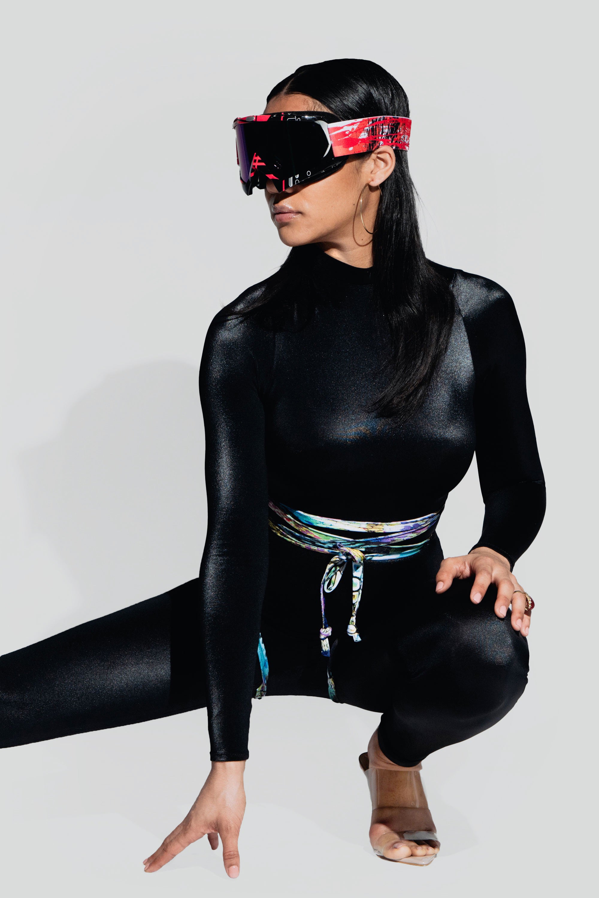 Person wearing a black catsuit with a colorful accents and goggles on a plain background