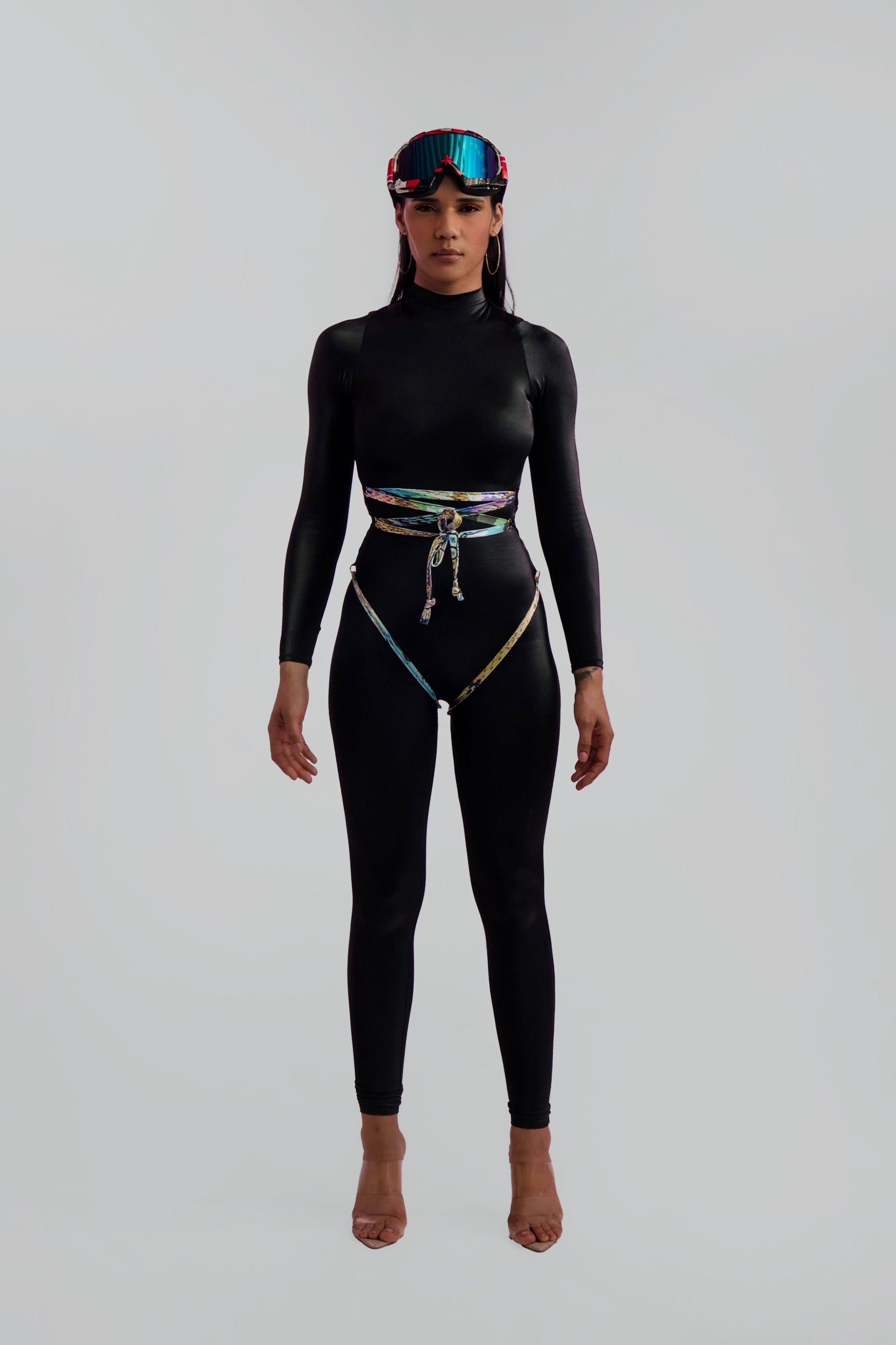 Person wearing a black catsuit with colorful accents and goggles on a white background