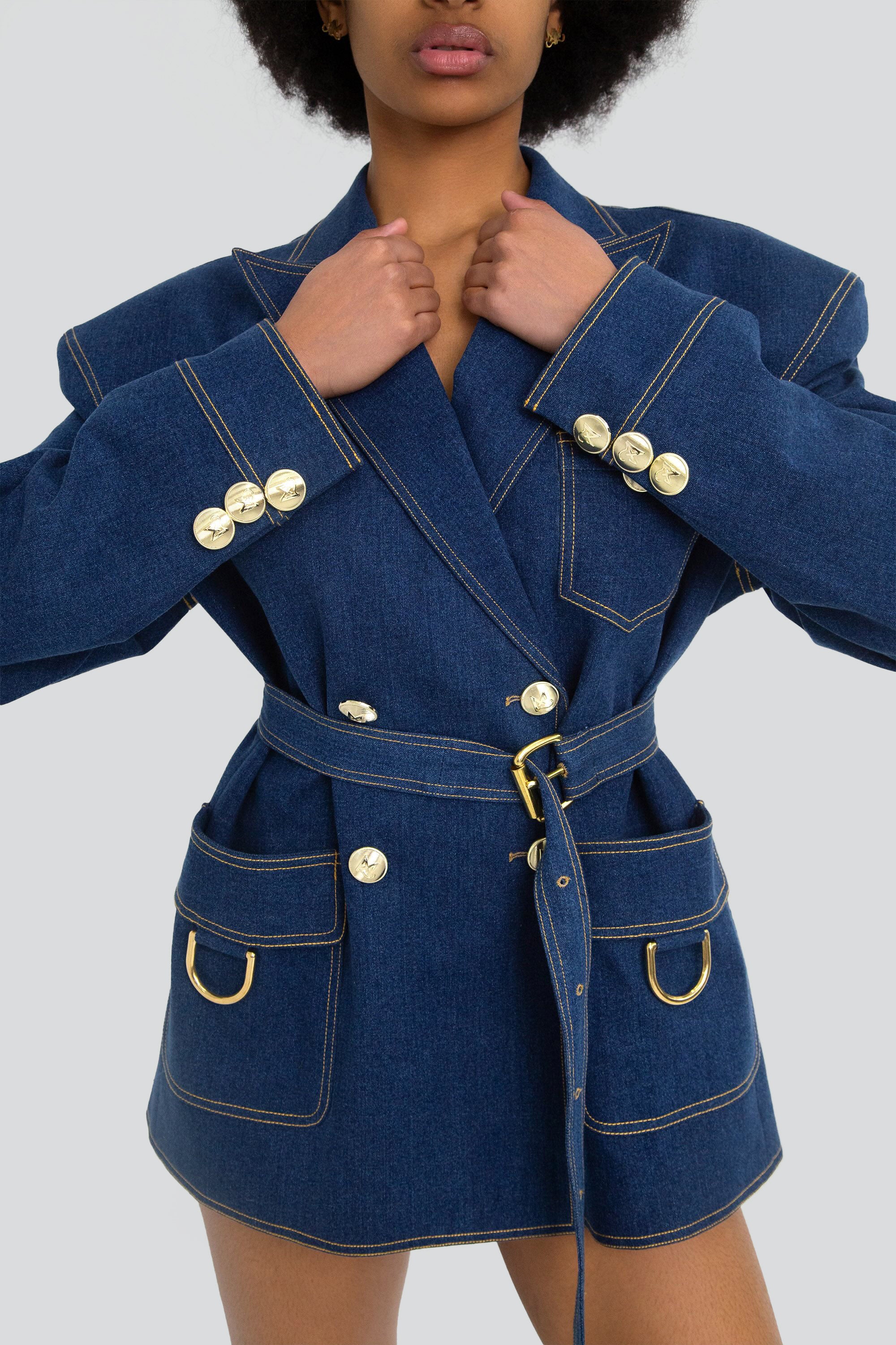 Woman wearing a blue denim blazer with gold hardware on a plain background
