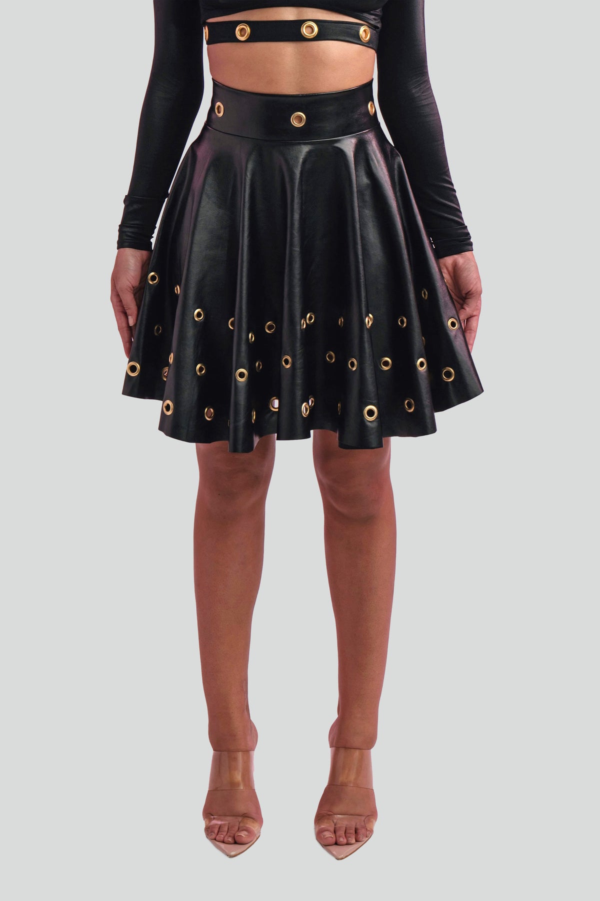 Close up view of sleek black faux leather fabric highlighting the metallic gold grommet accents along a tailored waistband