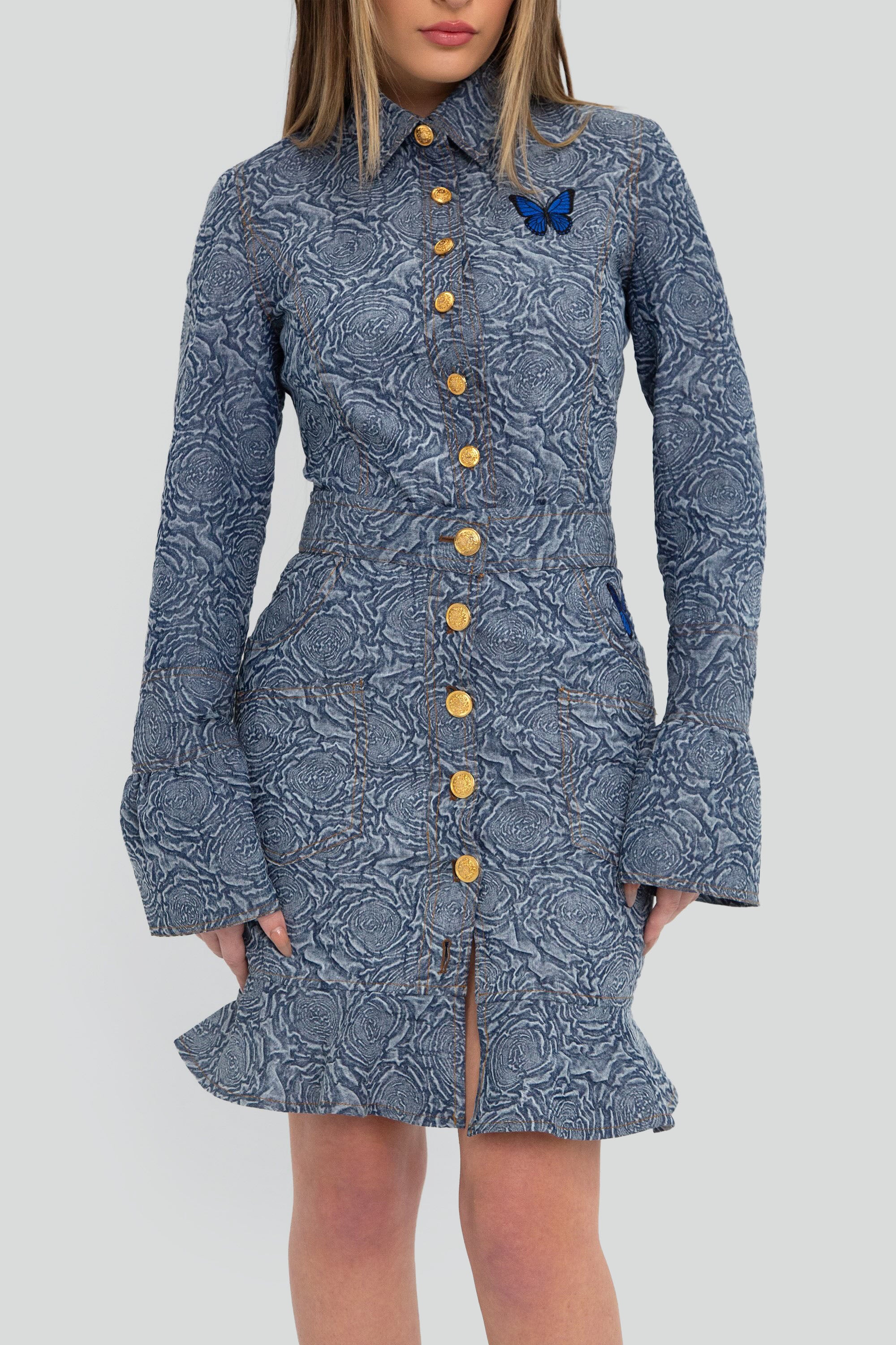 Woman wearing a blue patterned button up top and skirt set with flared sleeves on a plain background