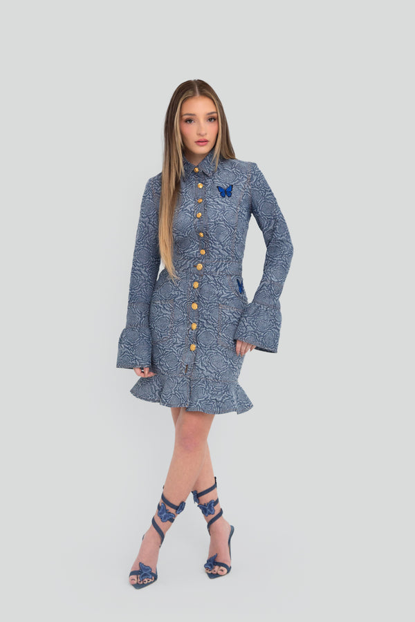 Woman wearing a blue patterned button up top and skirt set with flared sleeves on a plain background