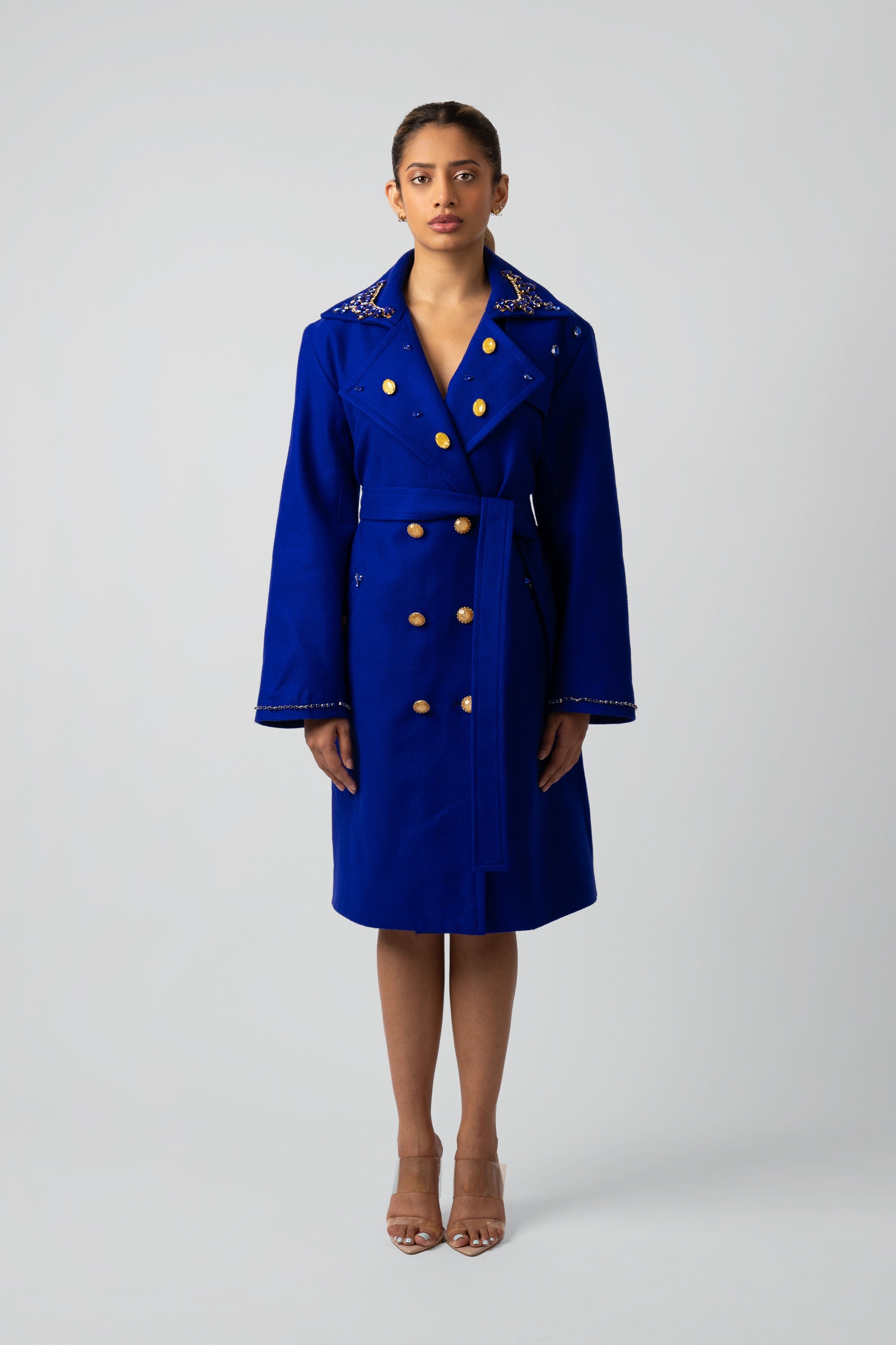 Woman wearing a blue trench coat with gold buttons and gold detailing on a white background