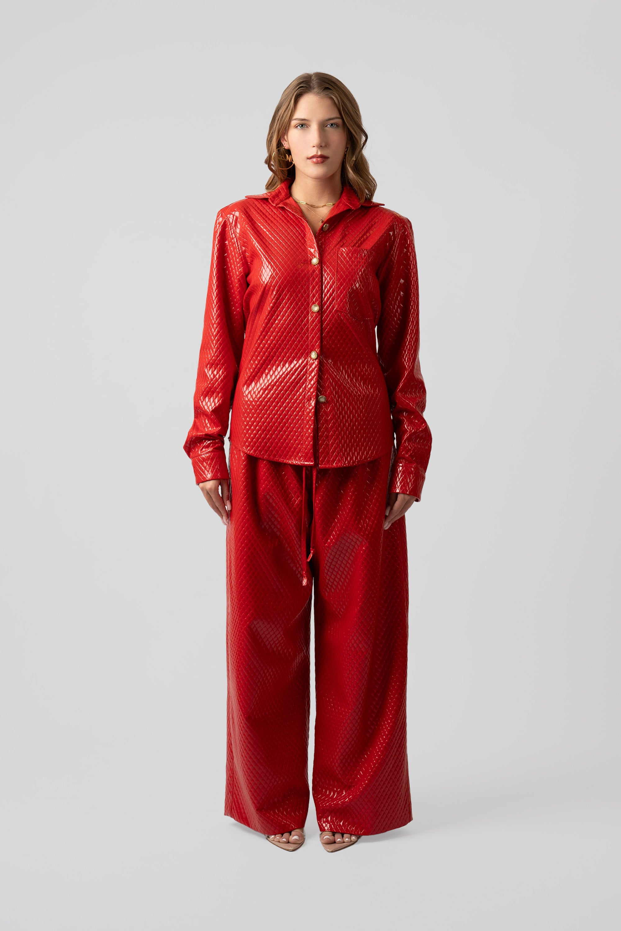 Woman wearing a red textured button up top and matching pants on a plain background