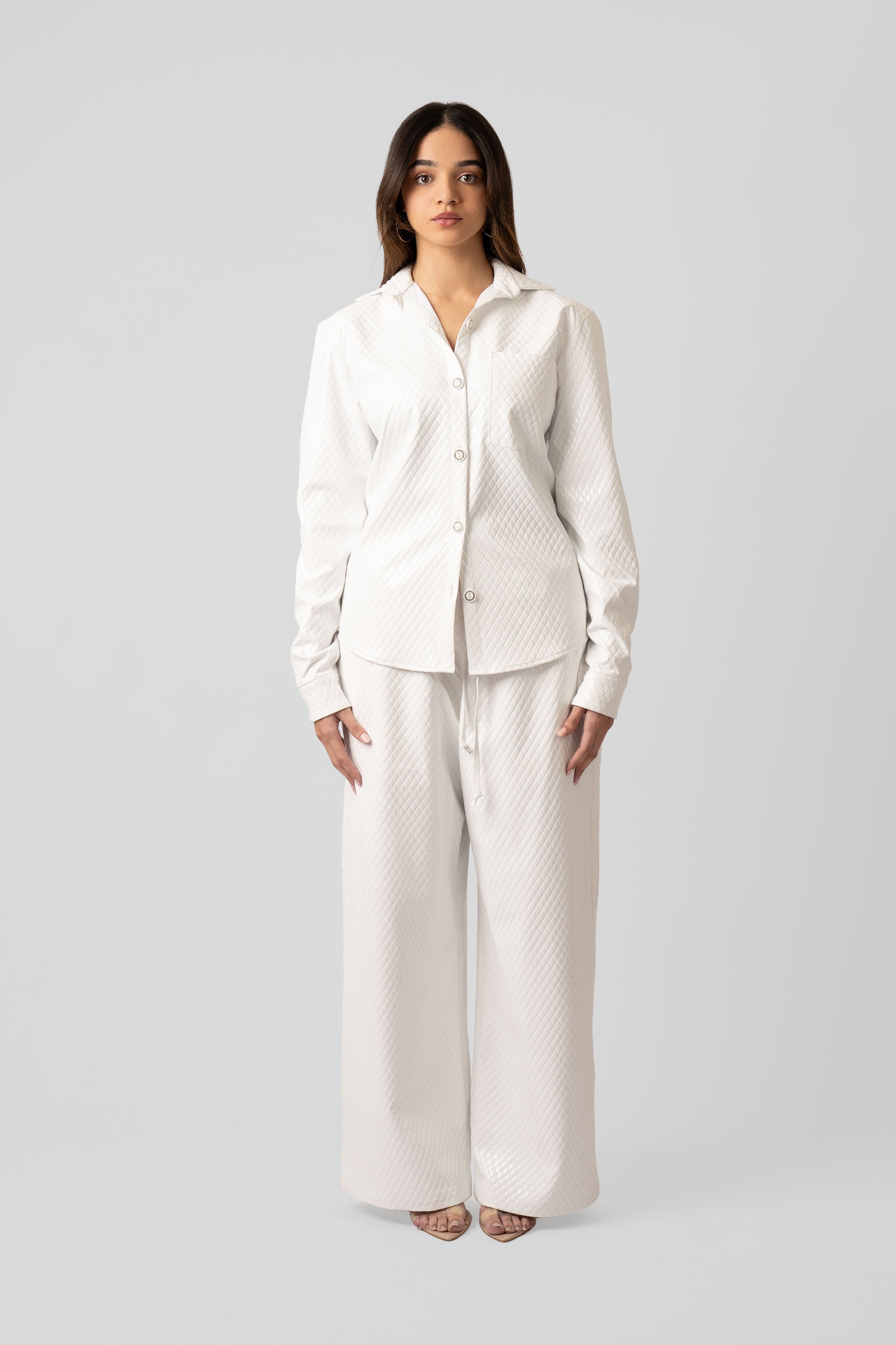 Woman wearing a white textured button up top and matching pants on a plain background