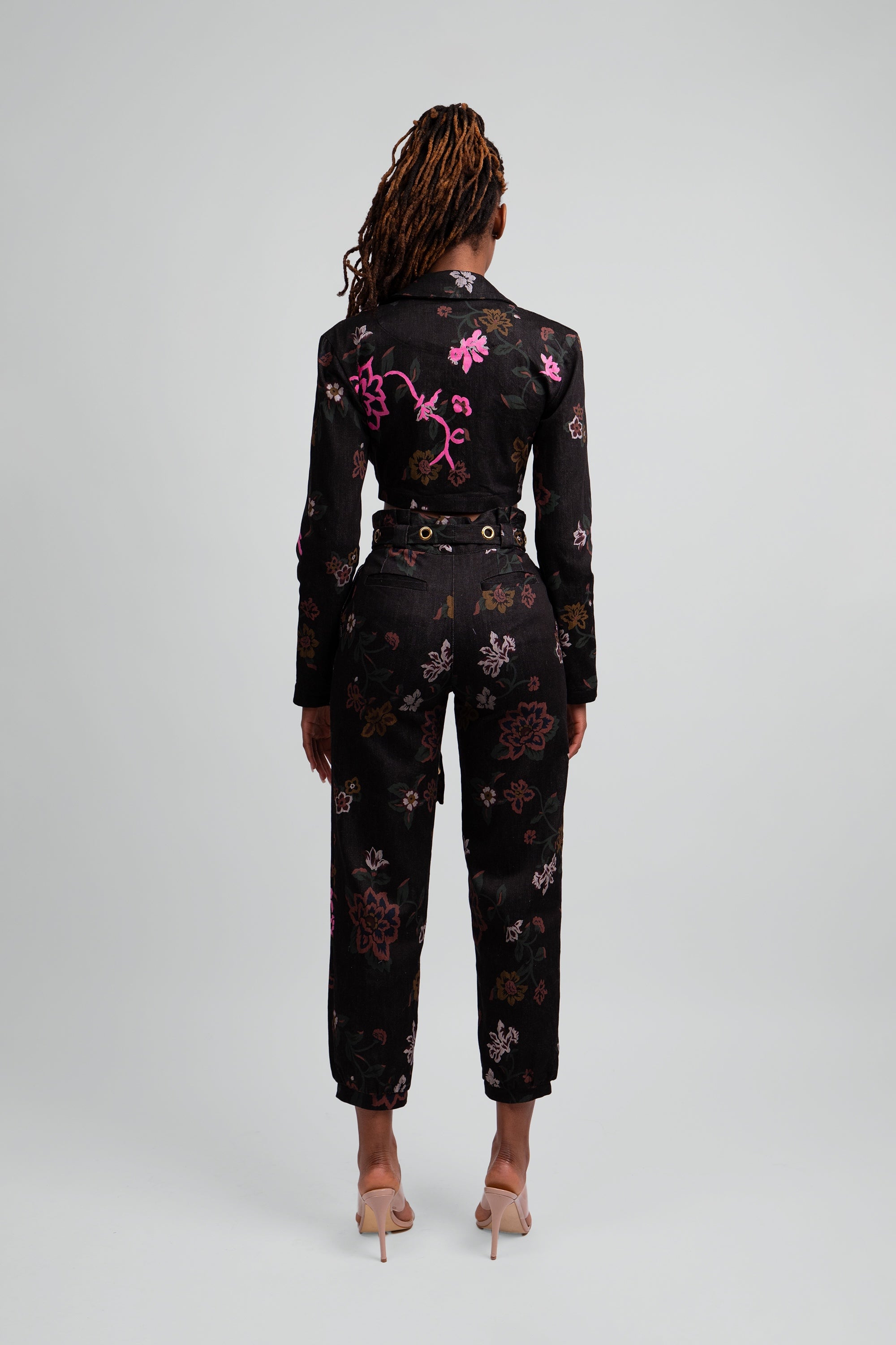 Back view of a woman wearing a black floral cropped suit set on a plain background