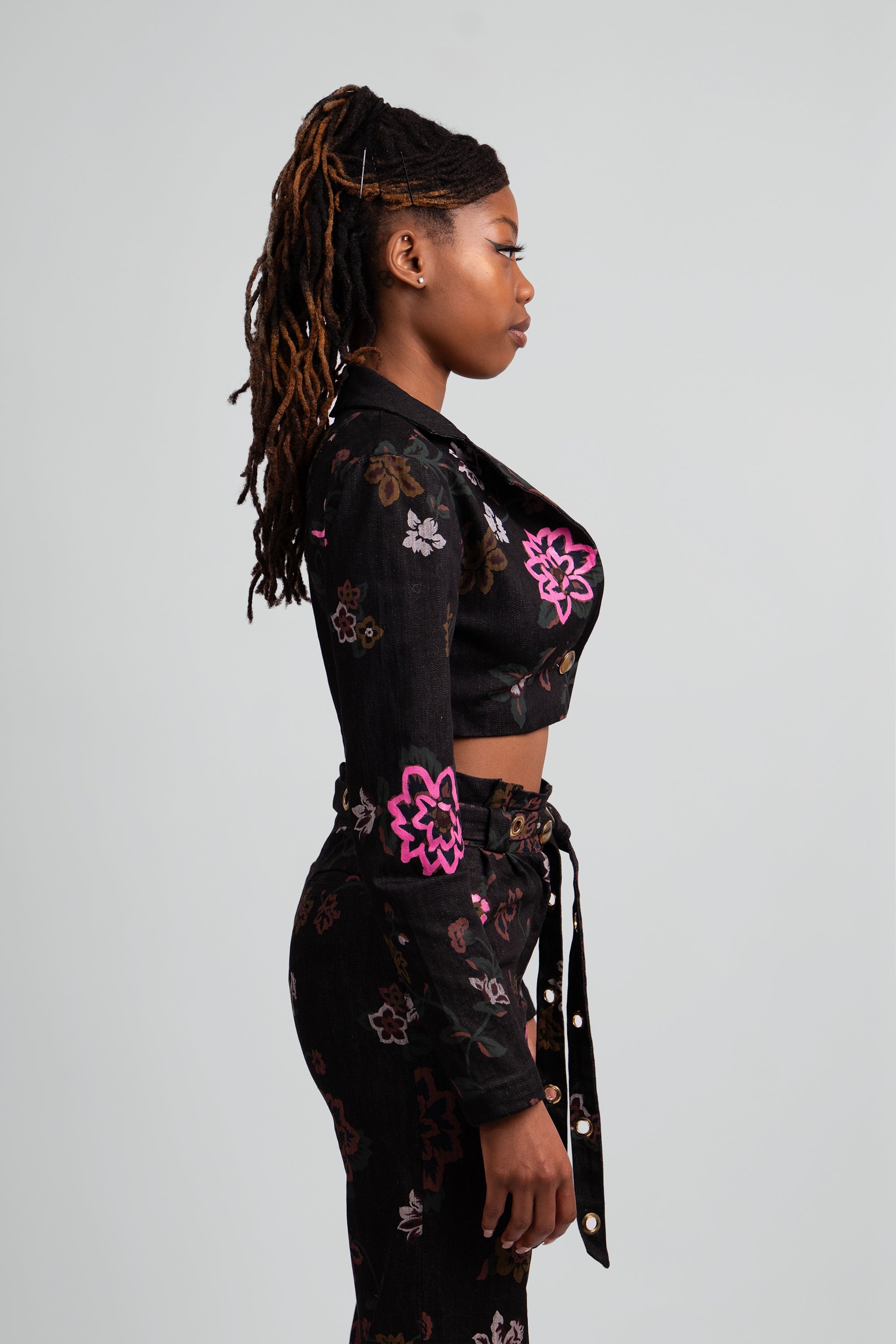 Close up side view of a woman wearing a black floral cropped suit set on a plain background