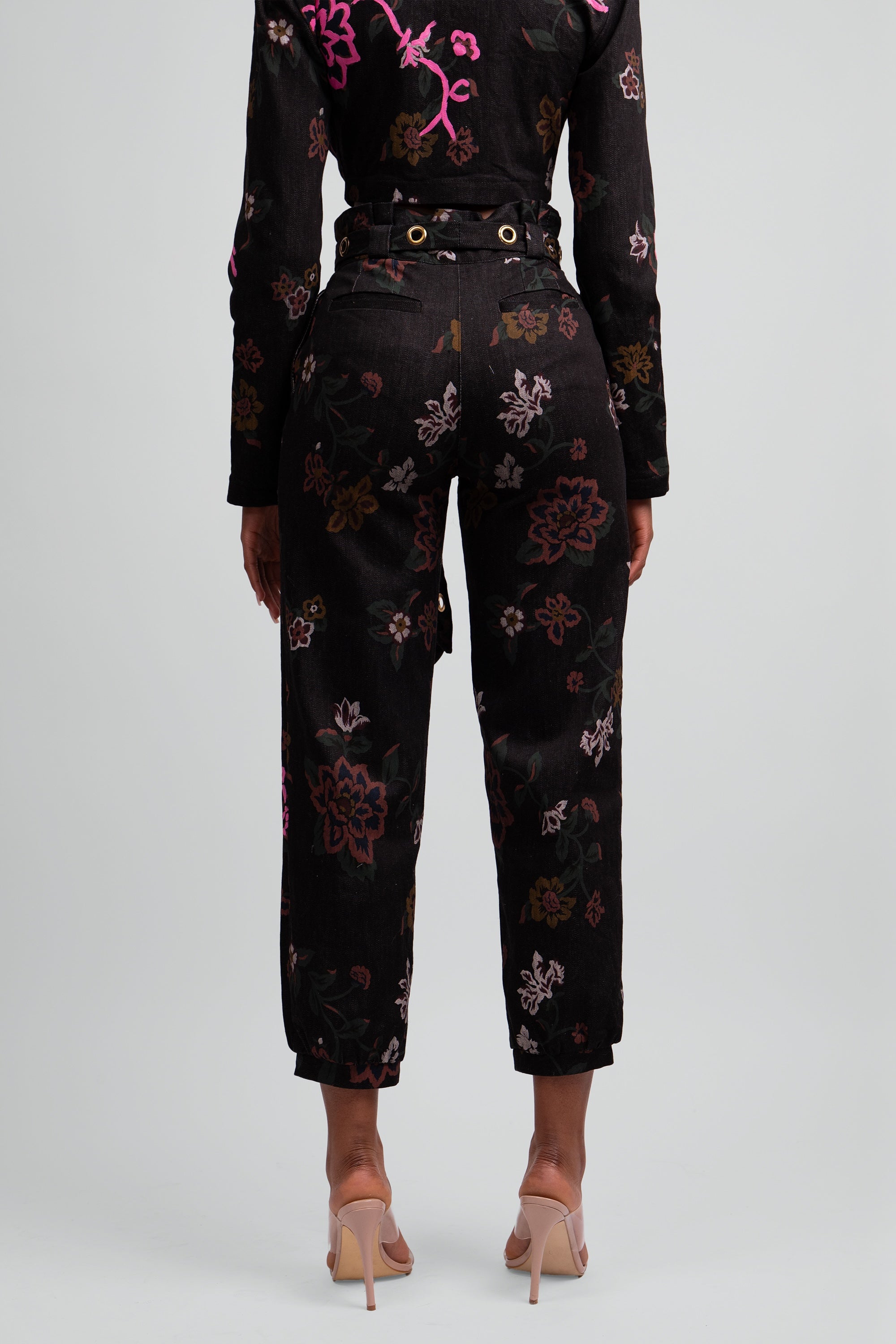 Close up back view of a black floral pant worn by a woman on a plain background