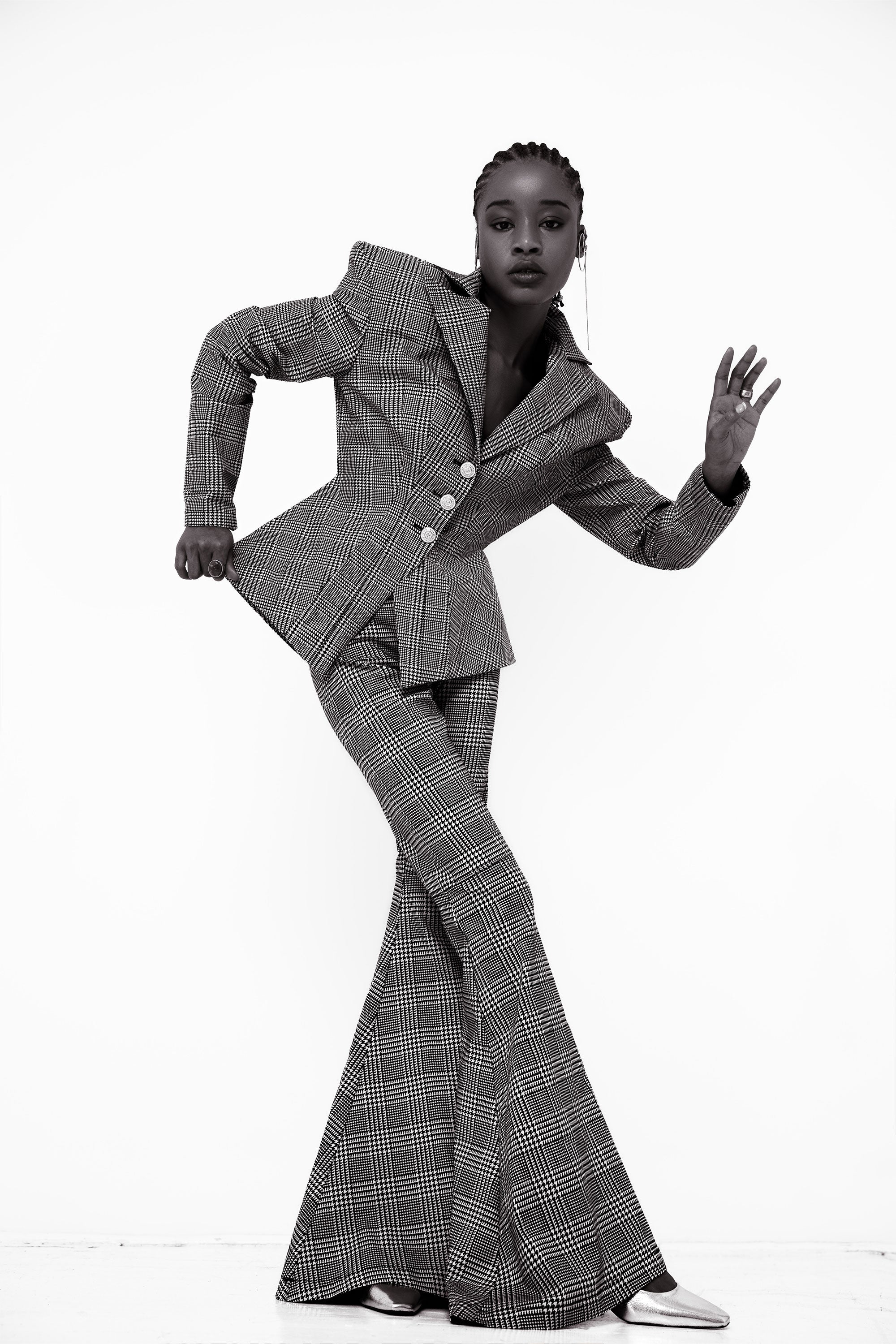 Woman wearing a gray plaid suit with flared pants posing against a white background