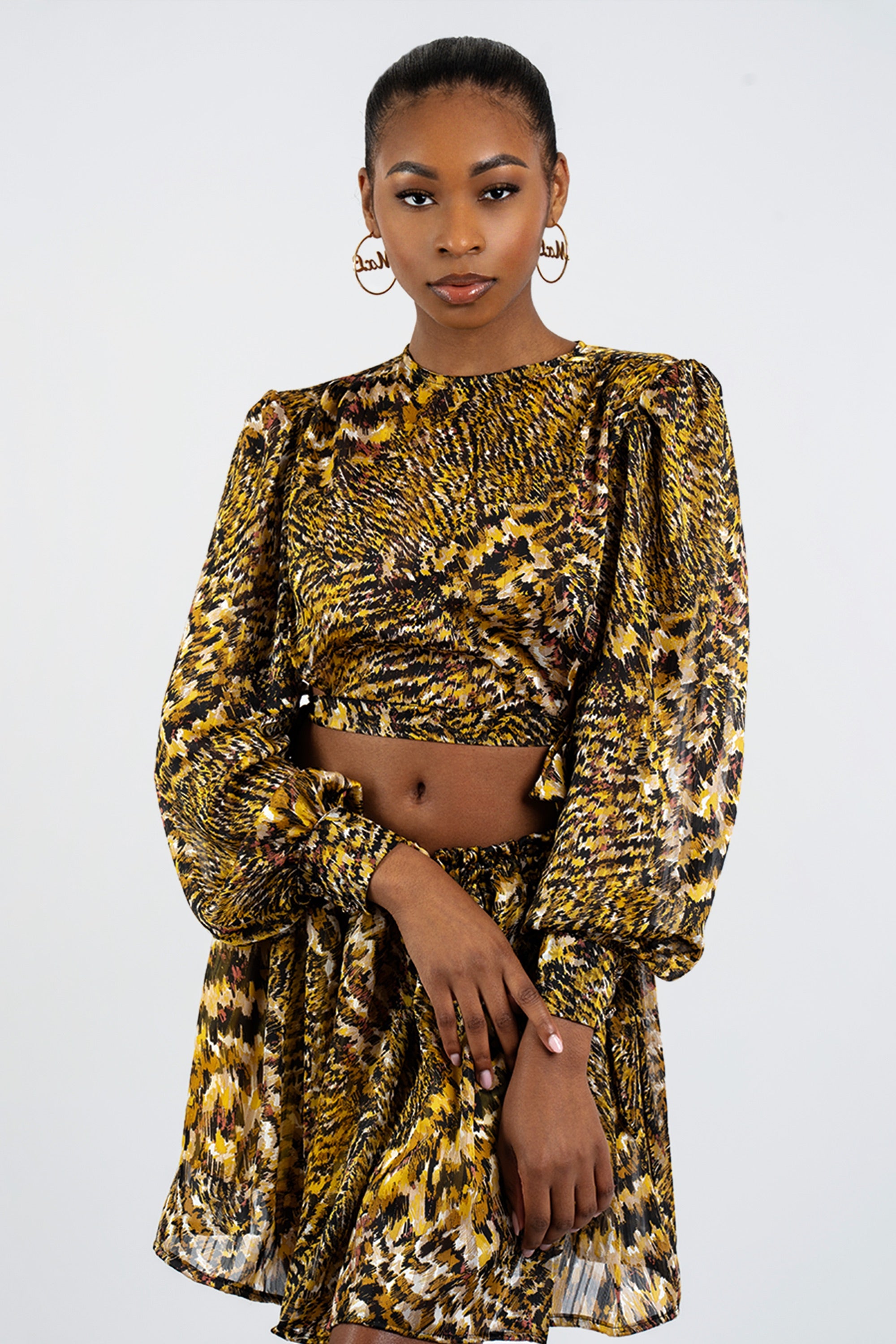 Woman wearing a gold and black patterned two-piece skirt set against a white background