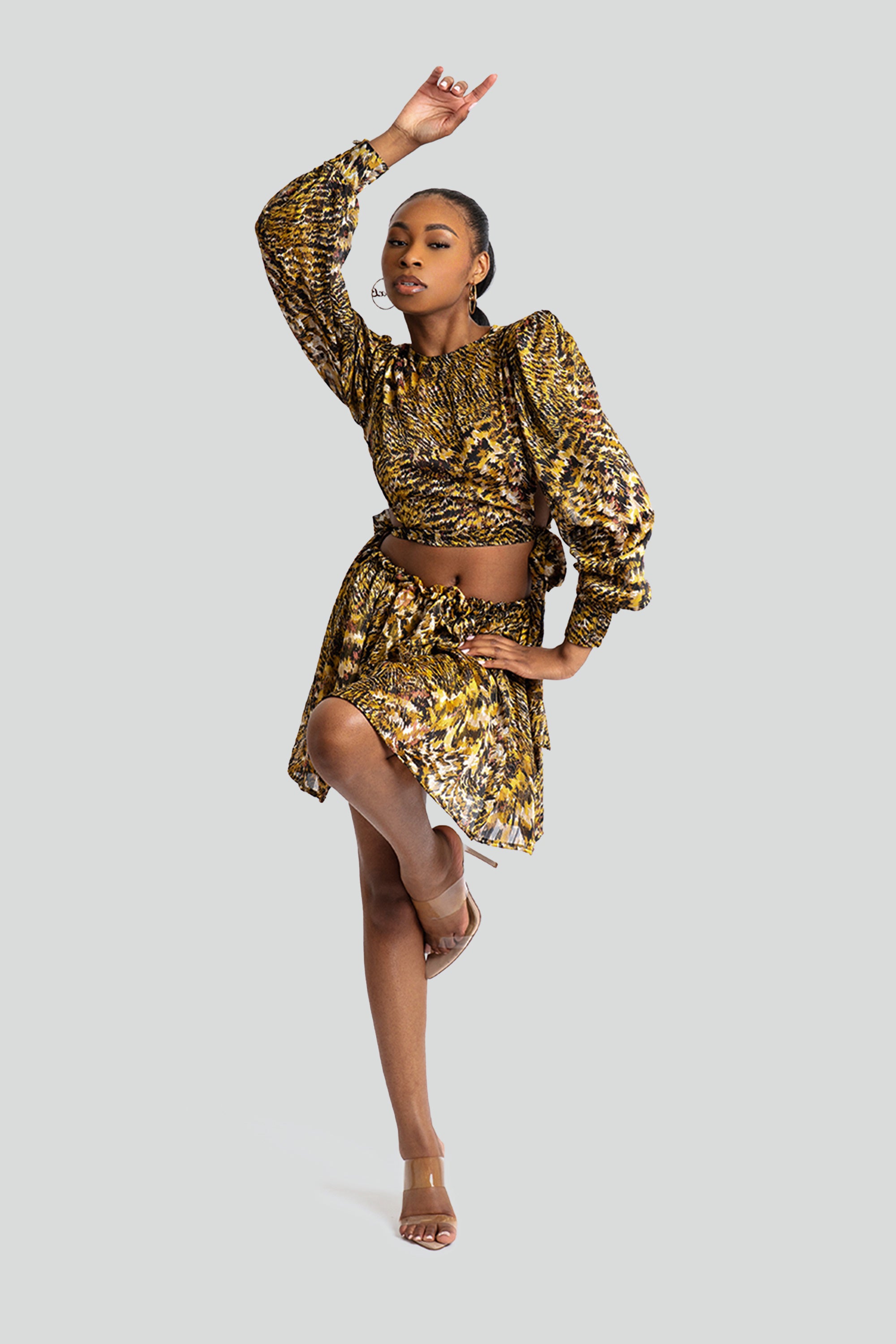 Woman in a gold and black patterned two-piece skirt set posing against a white background