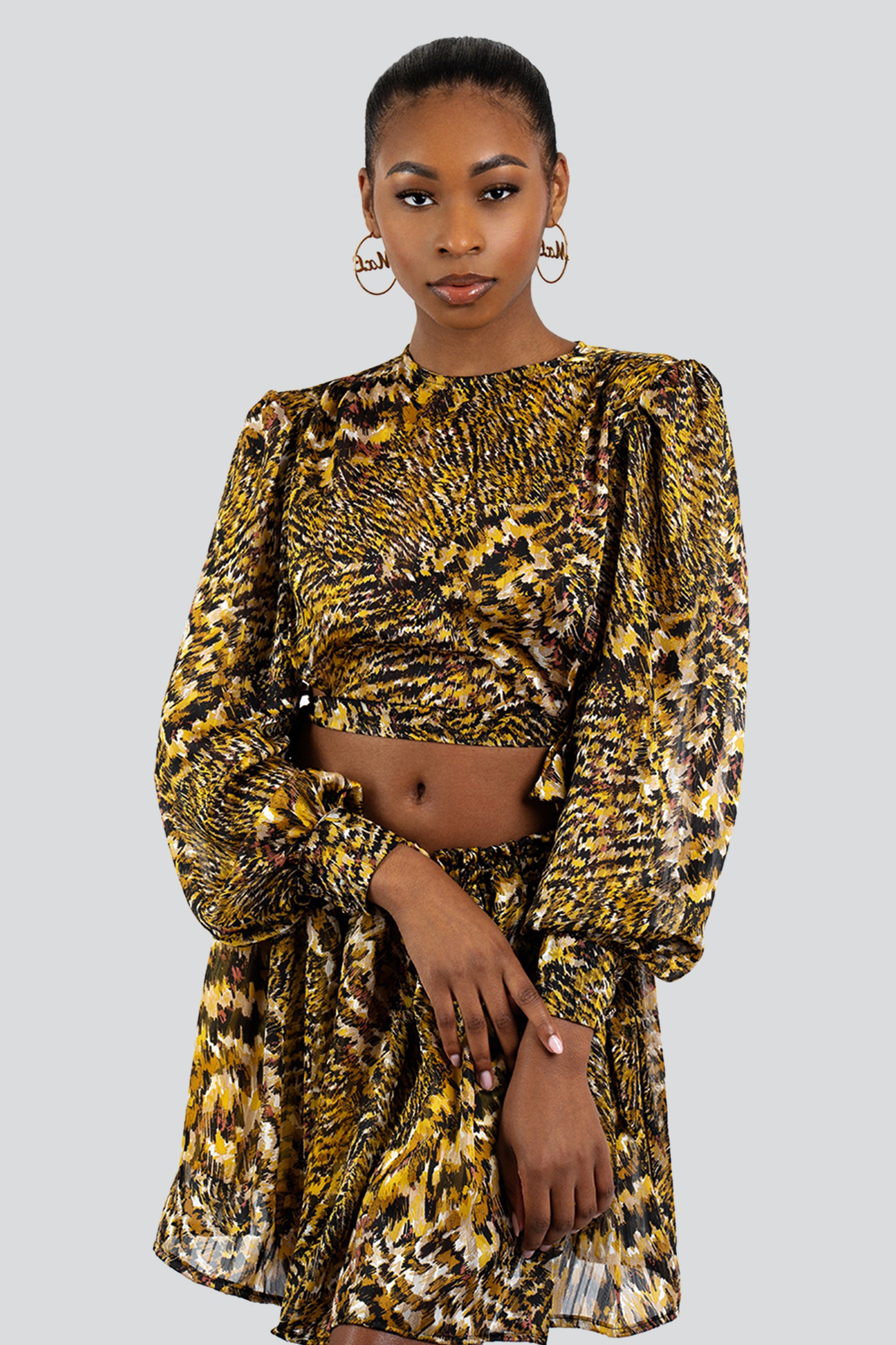 Woman wearing a gold and black patterned two-piece skirt set against a white background